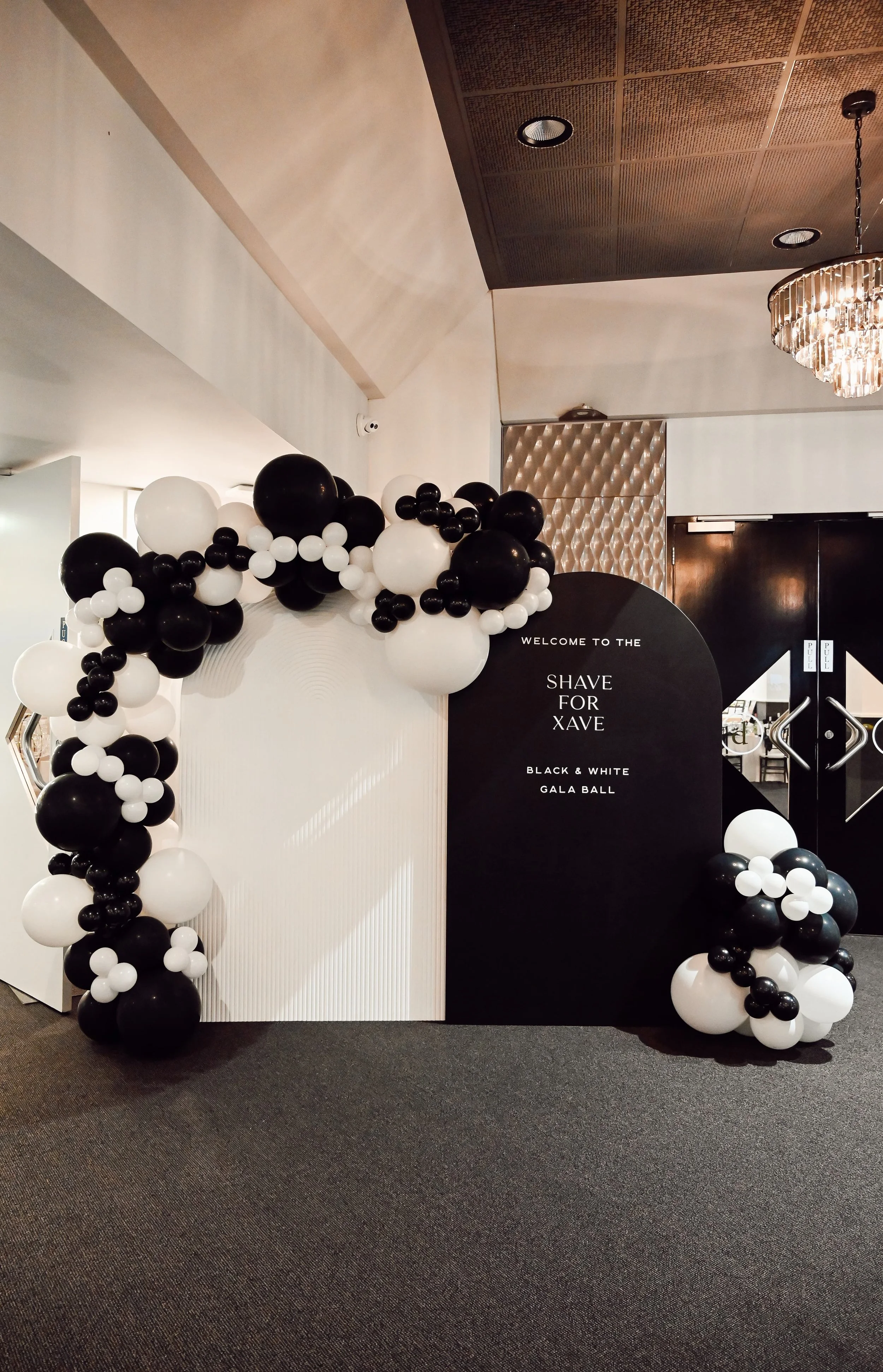 Black and white balloon arch and a black signboard at a Gala event titled "Shave for Xave" at Donato the venue in Adelaide