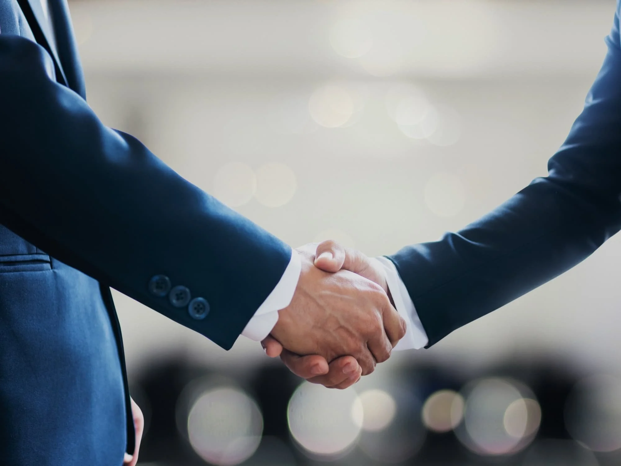 Two people in business suits shaking hands, symbolizing a greeting or agreement.