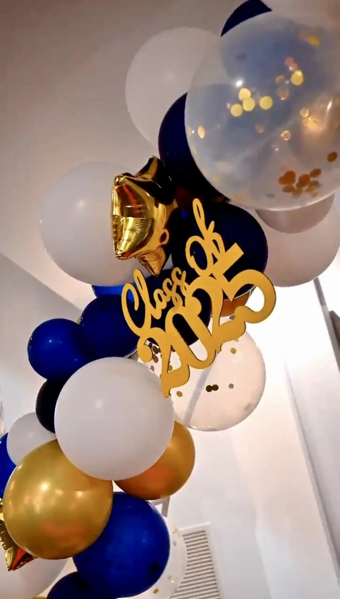 Balloon arch with black, white, navy blue, gold, and confetti balloons and a yellow 'Class of 2023' sign for graduation celebration.