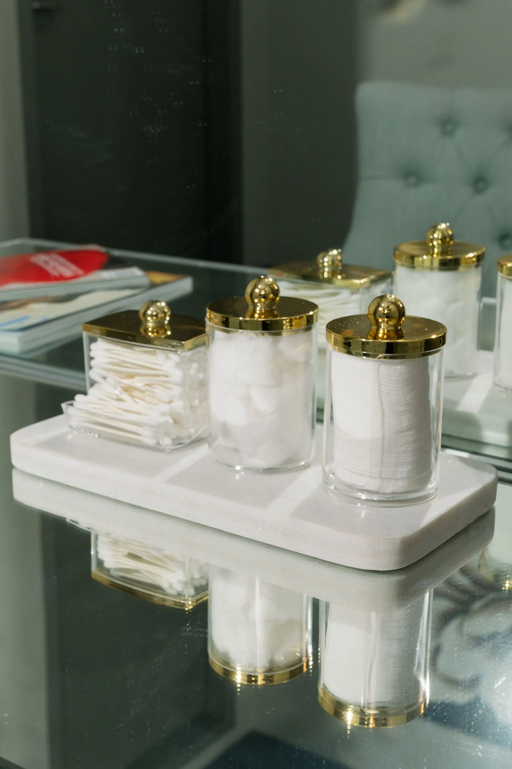 Collection of transparent containers with gold lids, holding cotton swabs, cotton balls, and possibly other cosmetic items, arranged on a white marble tray at Donato the venue in Adelaide