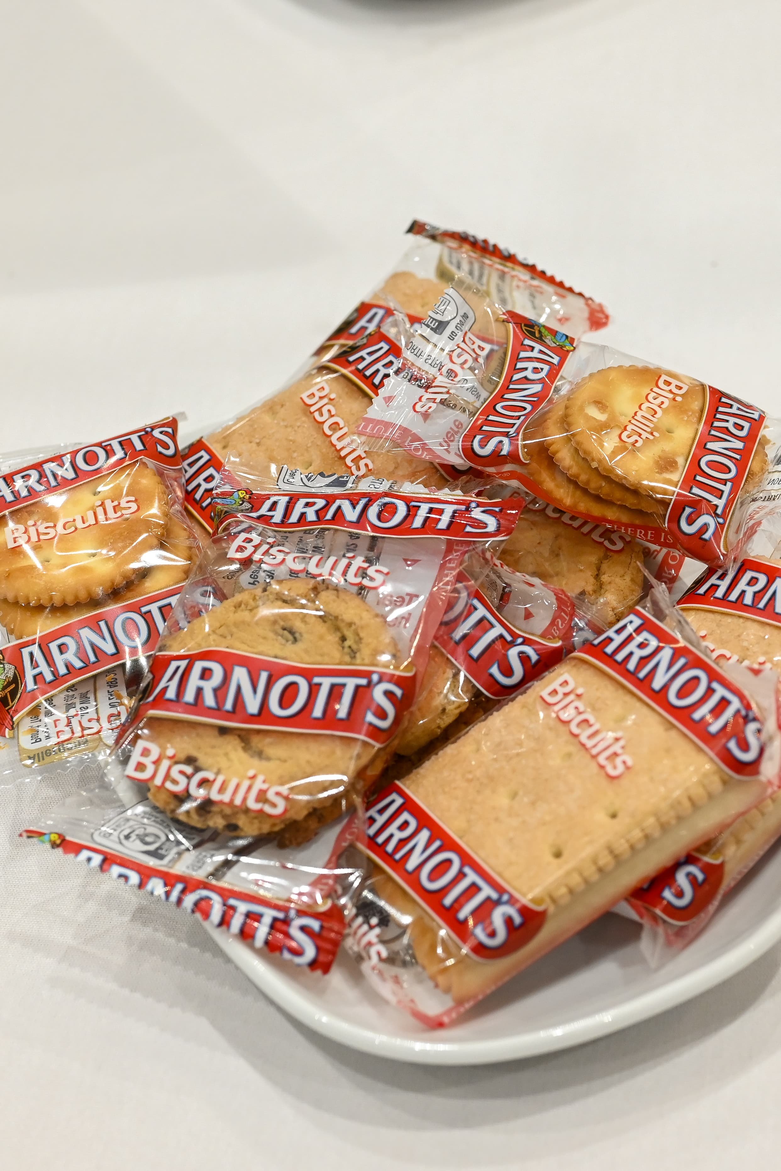 A white bowl containing individually wrapped Arnotts biscuits, including cookies and digestive biscuits.