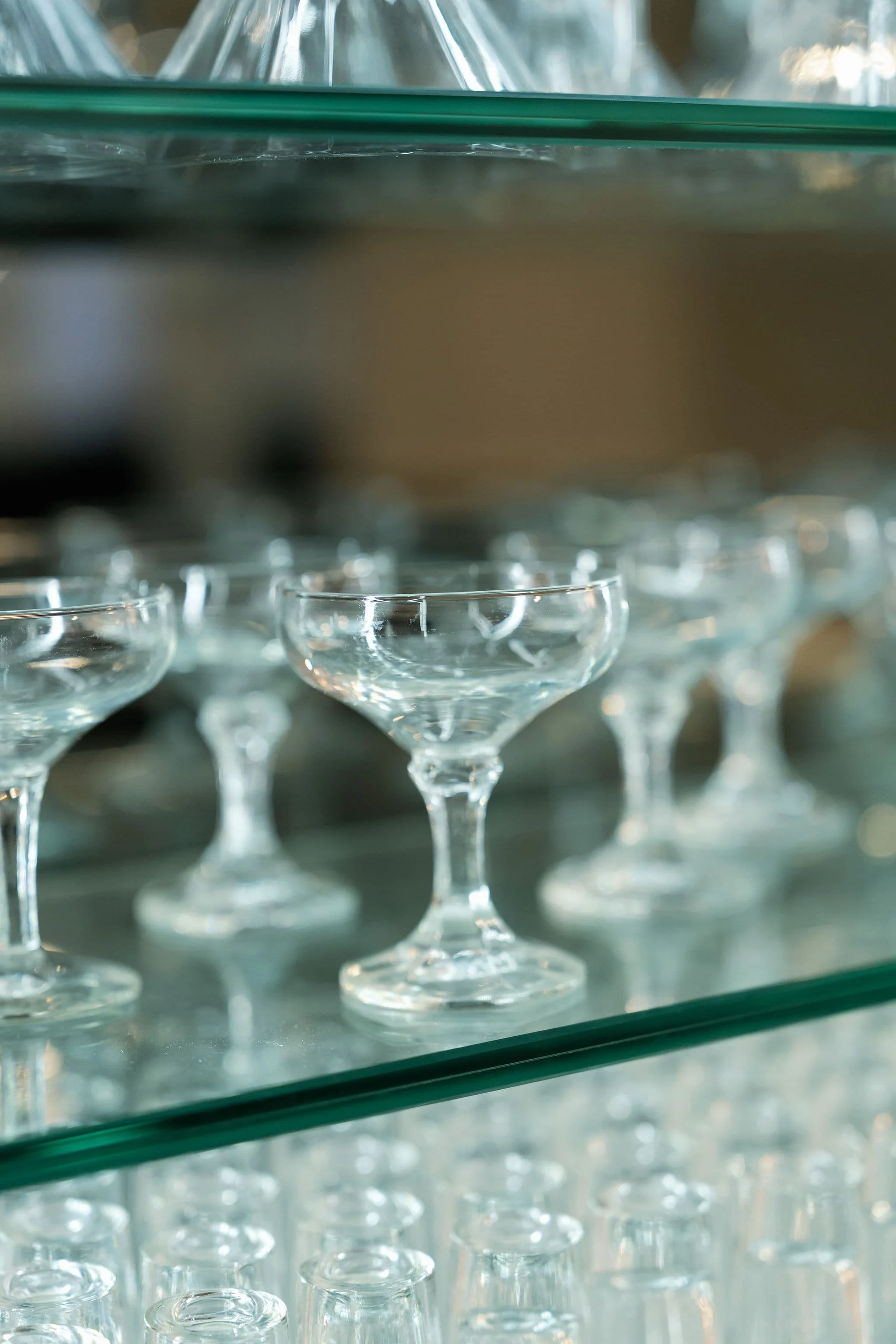 Multiple empty shot glasses on a glass shelf, viewed from below.