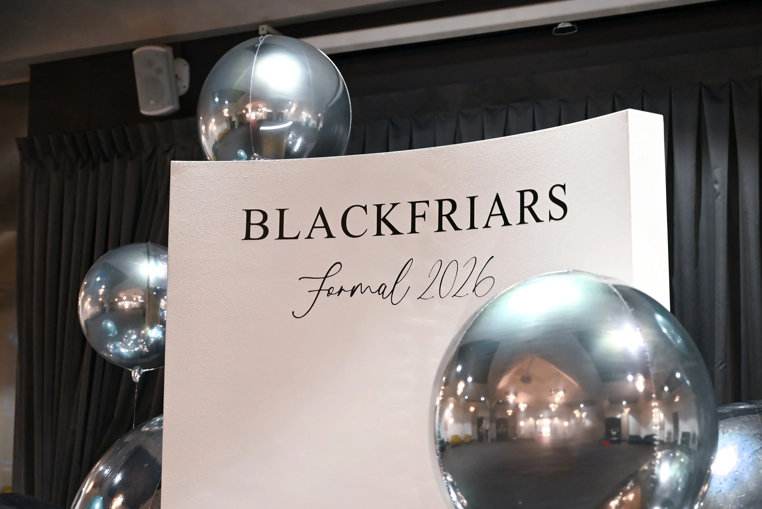 A sign with the word "Blackfriars" and the year "2026" underneath, surrounded by silver balloons at a formal event.