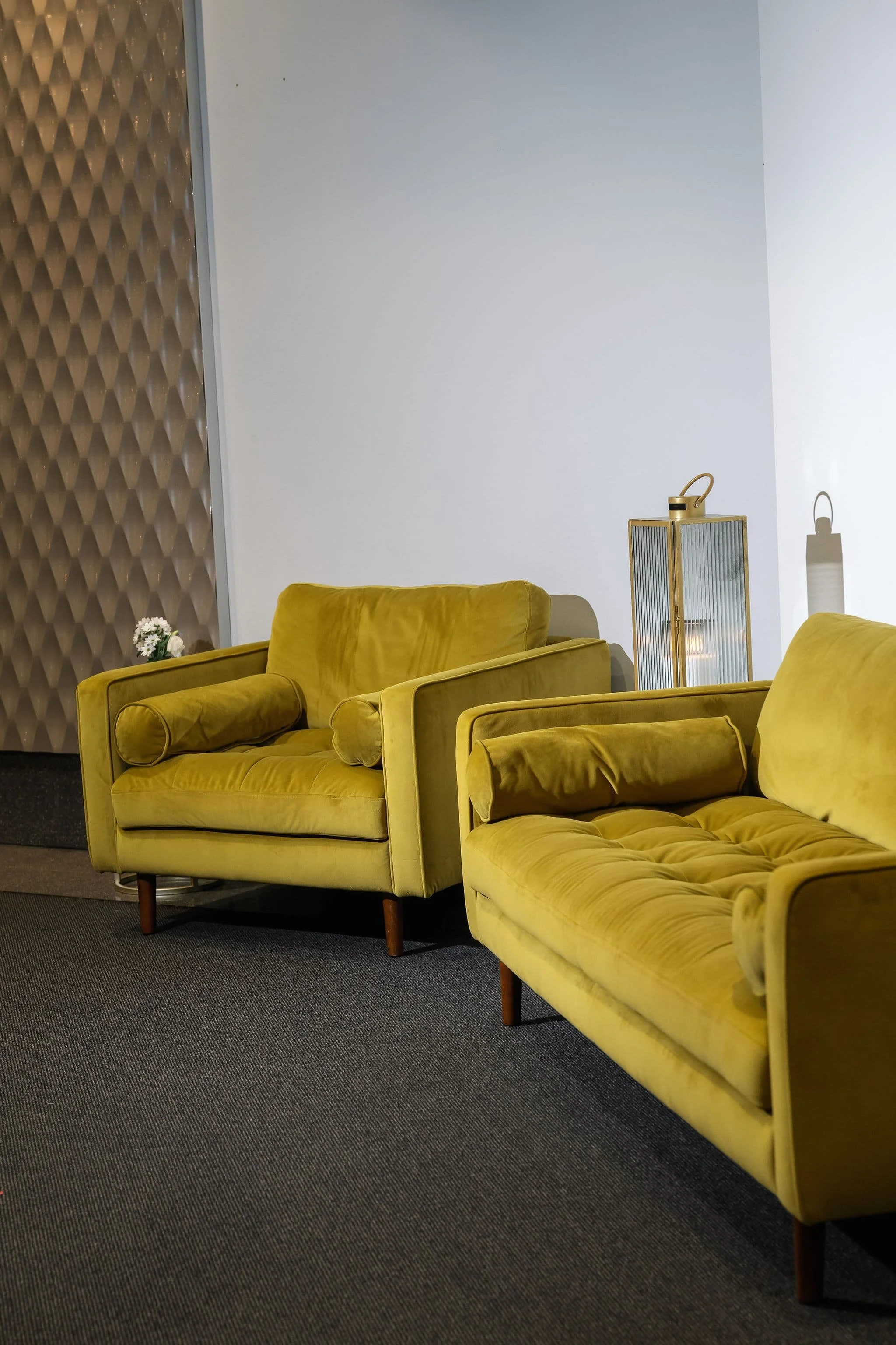 Yellow velvet sofas in a modern lounge with a textured wall and decorative lanterns.