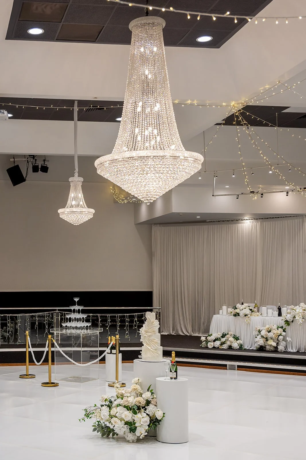 Elegant indoor wedding reception area with large crystal chandeliers, floral arrangements, and champagne bottles at Donato the venue in Adelaide