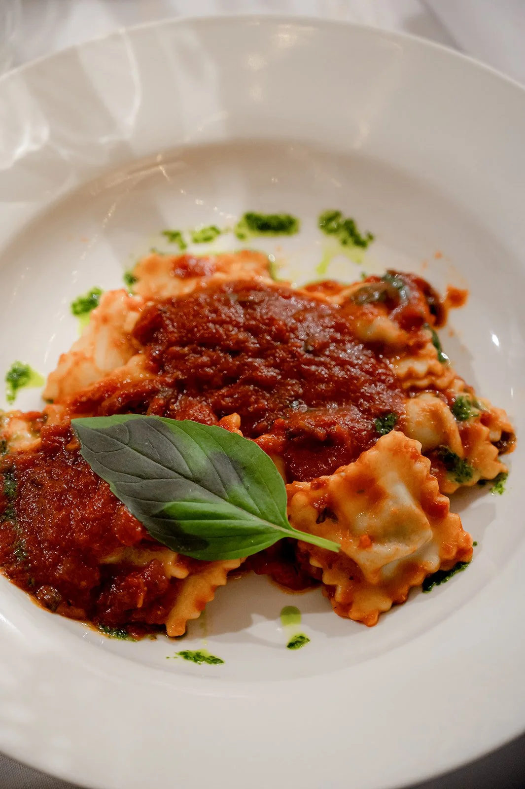 Plate of ravioli pasta with tomato sauce, garnished with fresh basil leaves and a drizzle of green oil.