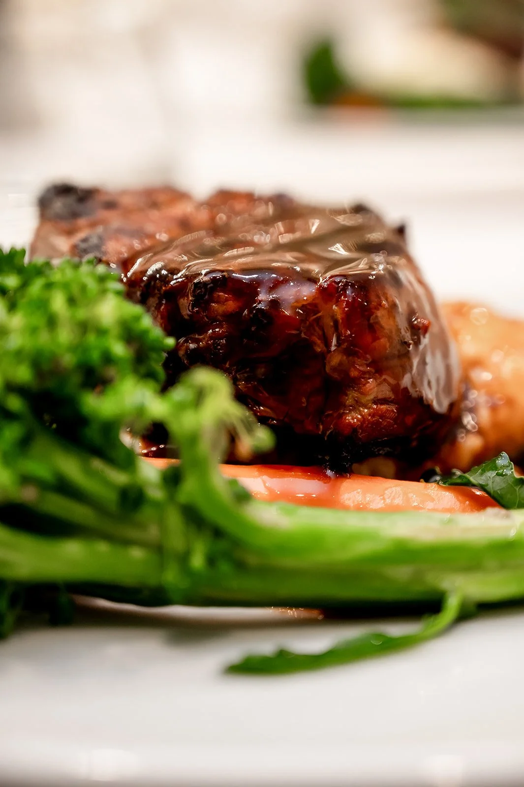 Close-up of a glazed beef meatloaf with fresh greens and tomato slices on a white plate.