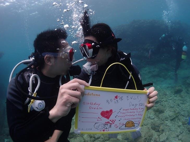 Two people in scuba diving gear underwater, holding a whiteboard with drawings and notes.