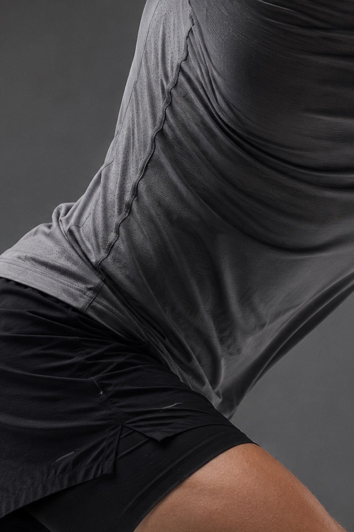 Close-up of a person wearing a gray textured hoodie and black shorts, sitting on a dark surface.