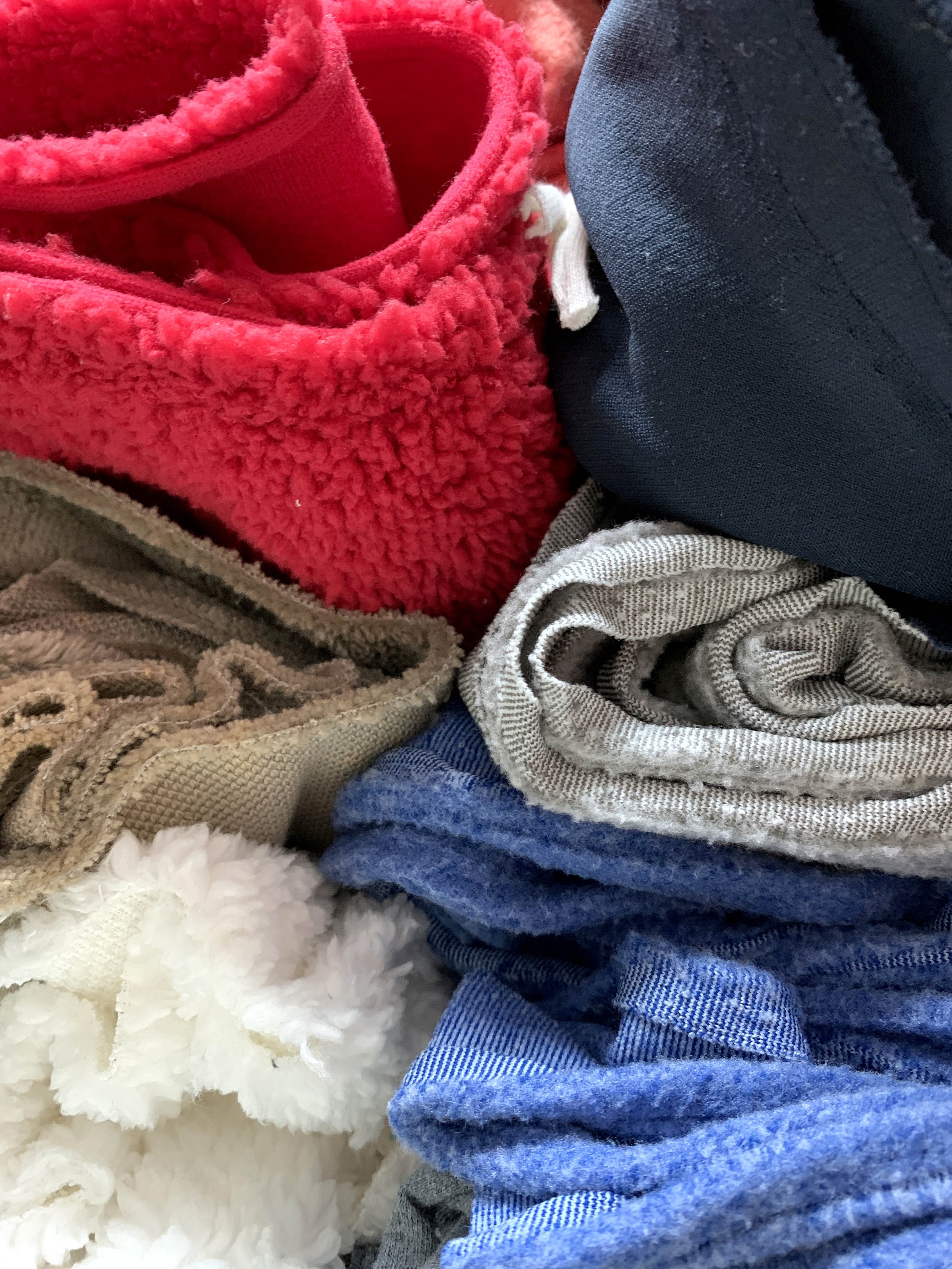 Close-up of various clothing items, including red fleece, black fabric, beige striped fabric, blue denim, and white fluffy material.