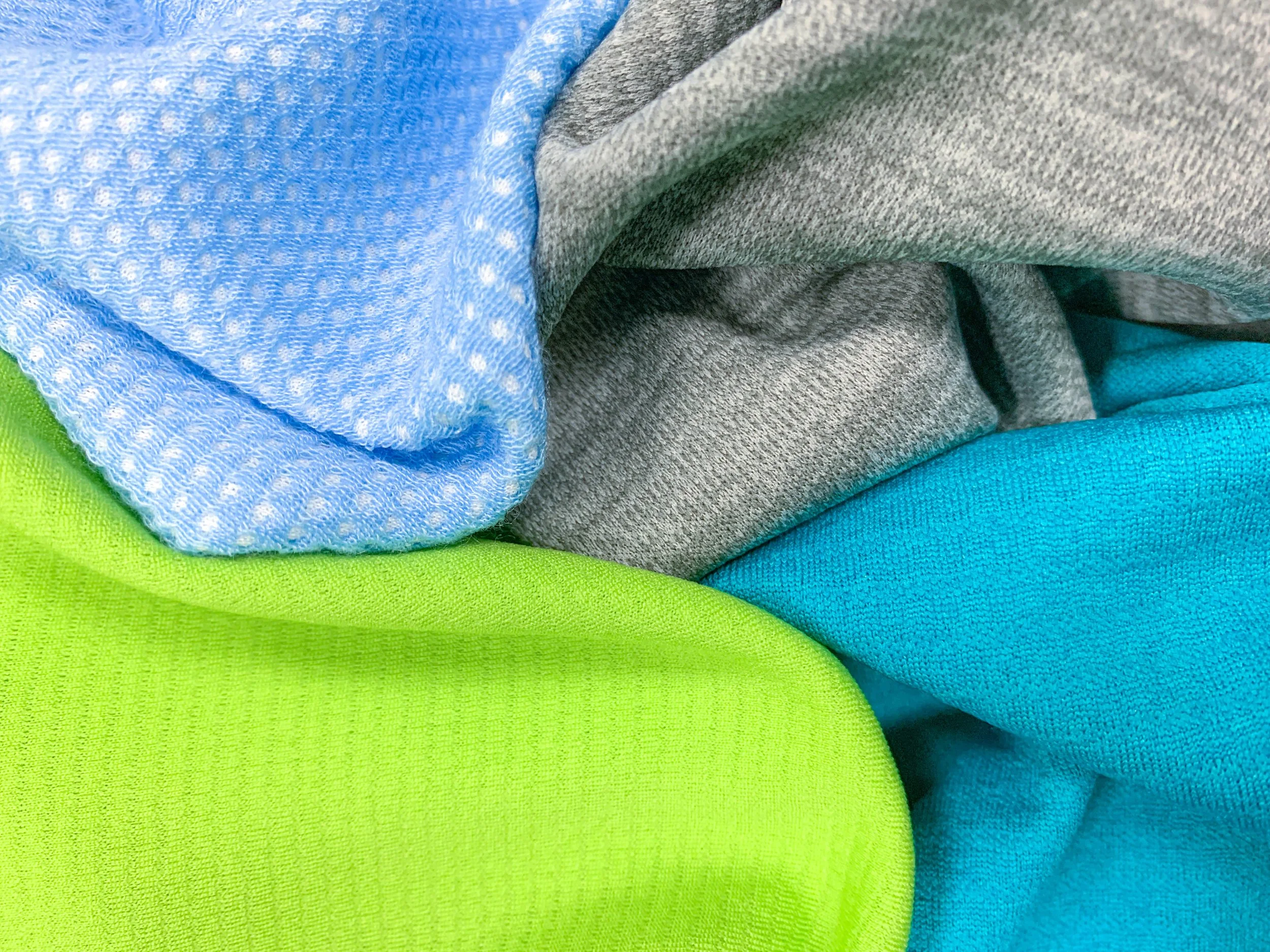 DaFon Textile close-up of folded colorful fabric, including blue, gray, teal, and bright green materials.