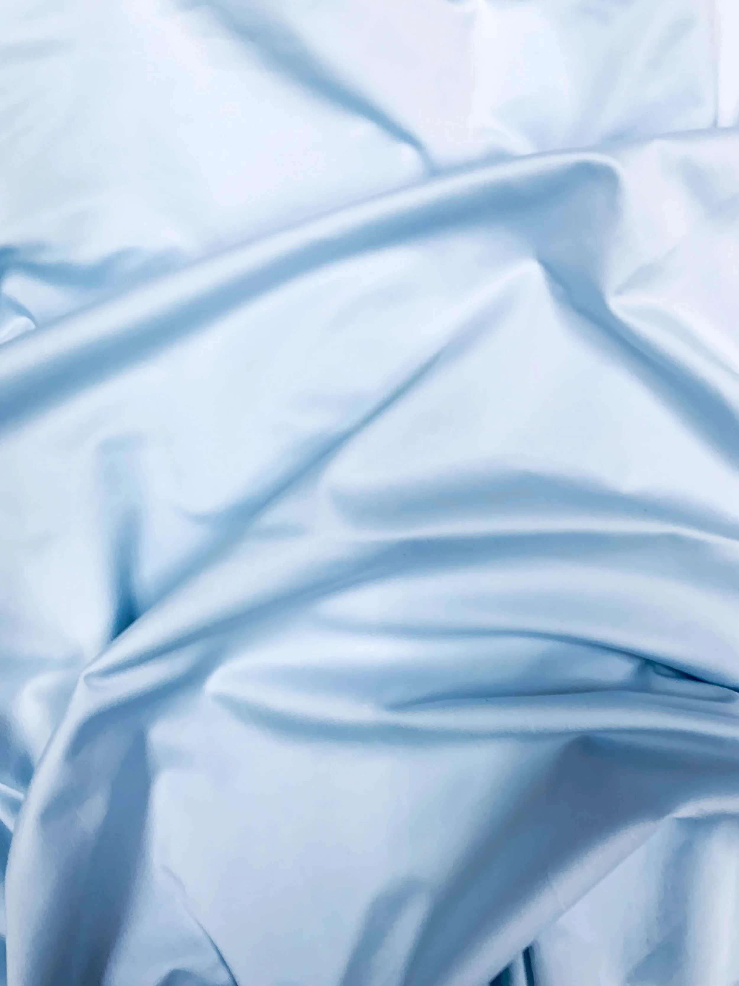 Close-up of light blue satin or silk fabric with soft folds and creases.