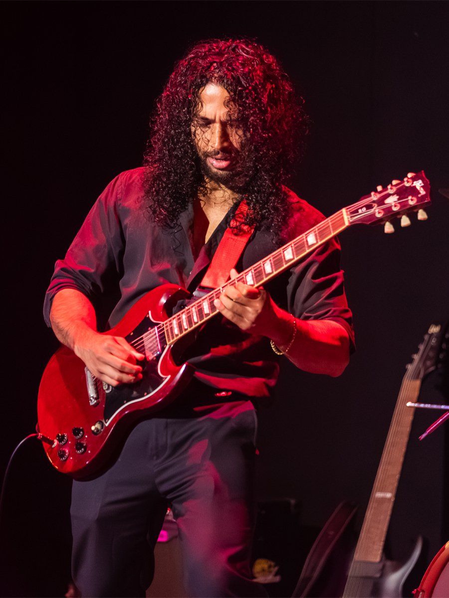 Musician with curly hair playing red electric guitar on stage.
