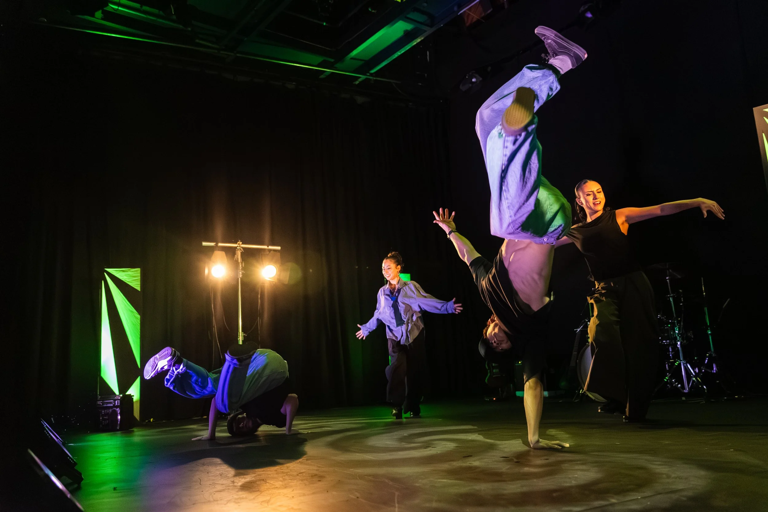 Performers practicing acrobatic dance on stage with black background and green stage lights.