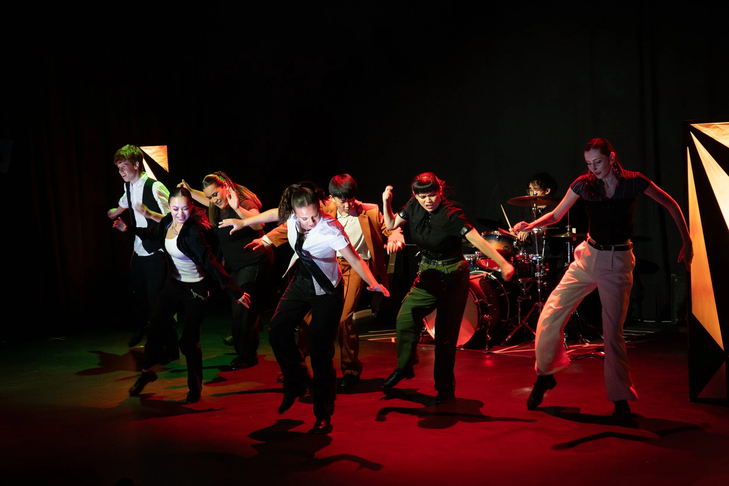 Group of dancers performing on stage with dark background and stage lighting.