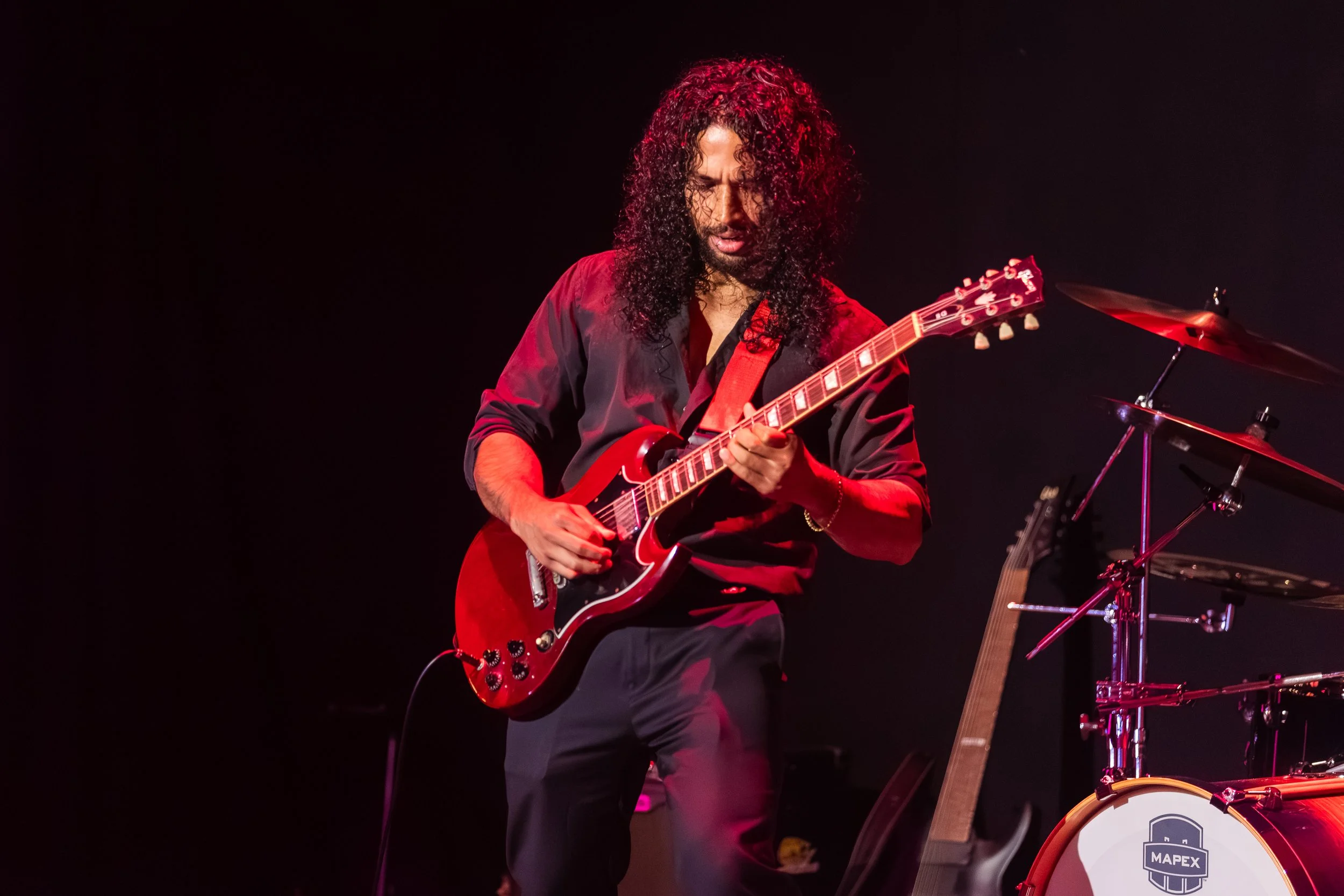A musician with curly hair playing an electric guitar on stage.