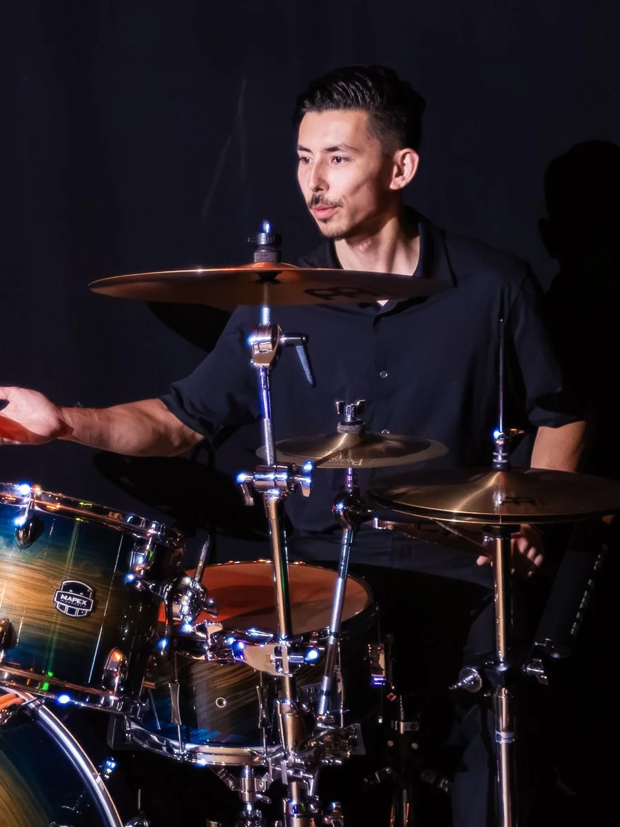 A man playing a drum set against a black background, focused on hitting the drums.