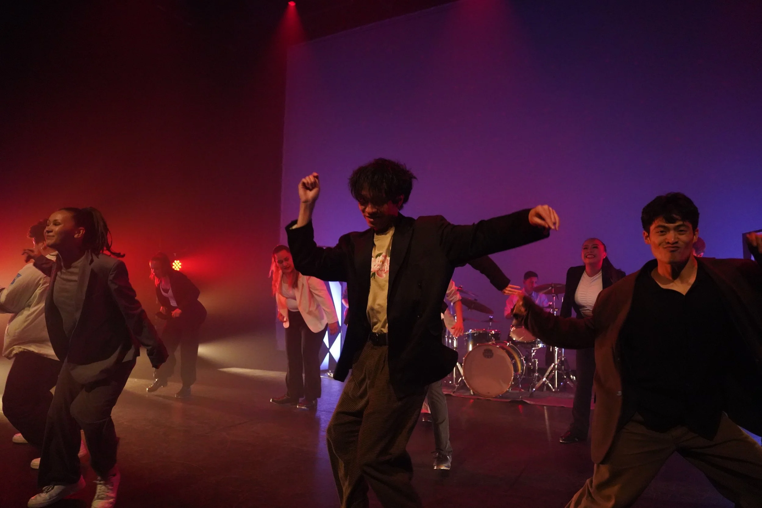 A group of diverse people dancing and enjoying themselves on stage with musical instruments in the background, under colorful stage lights.