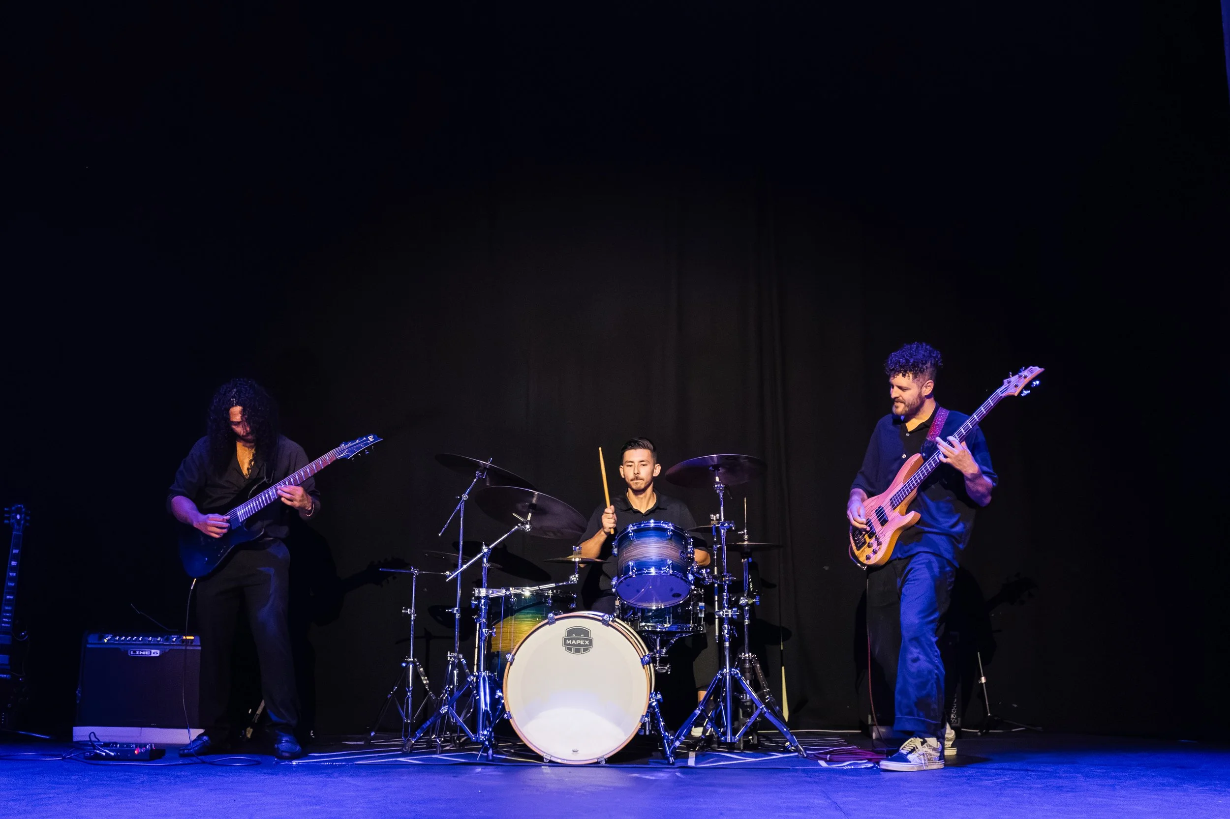 A band performing on stage with three musicians playing guitars and drums.