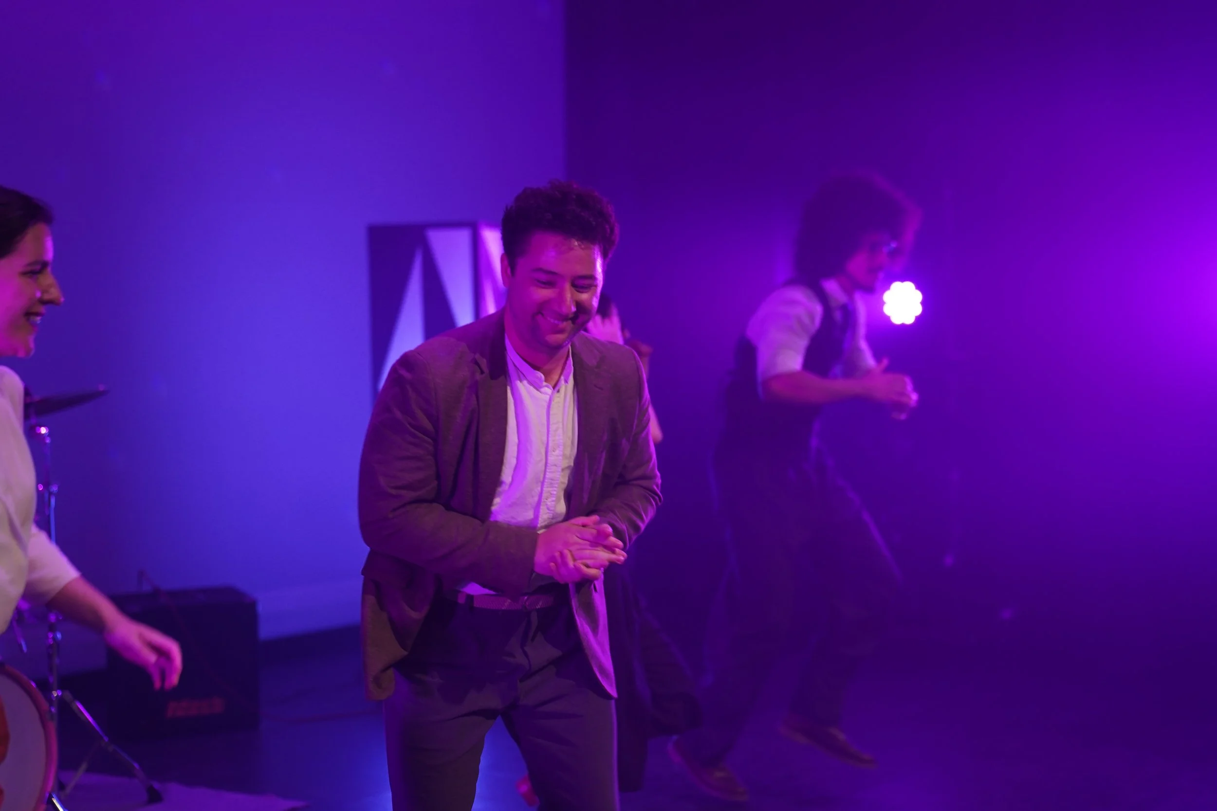Group of people, including a man in a blazer, participating in an event with purple stage lighting.