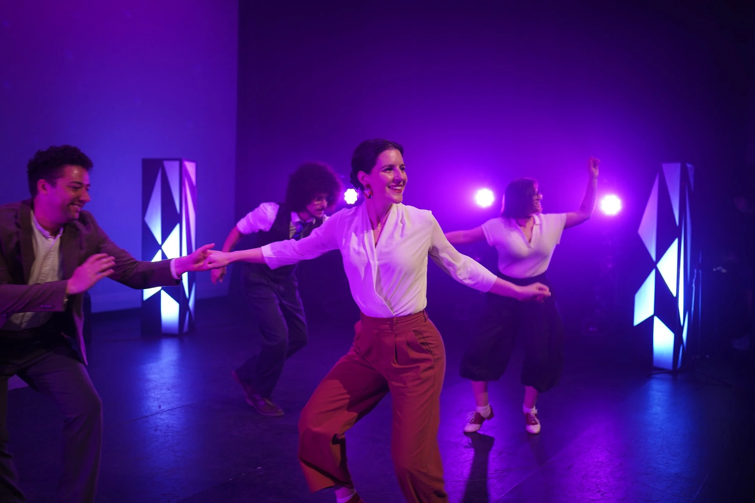 Group of people dancing and smiling on stage with purple lighting.