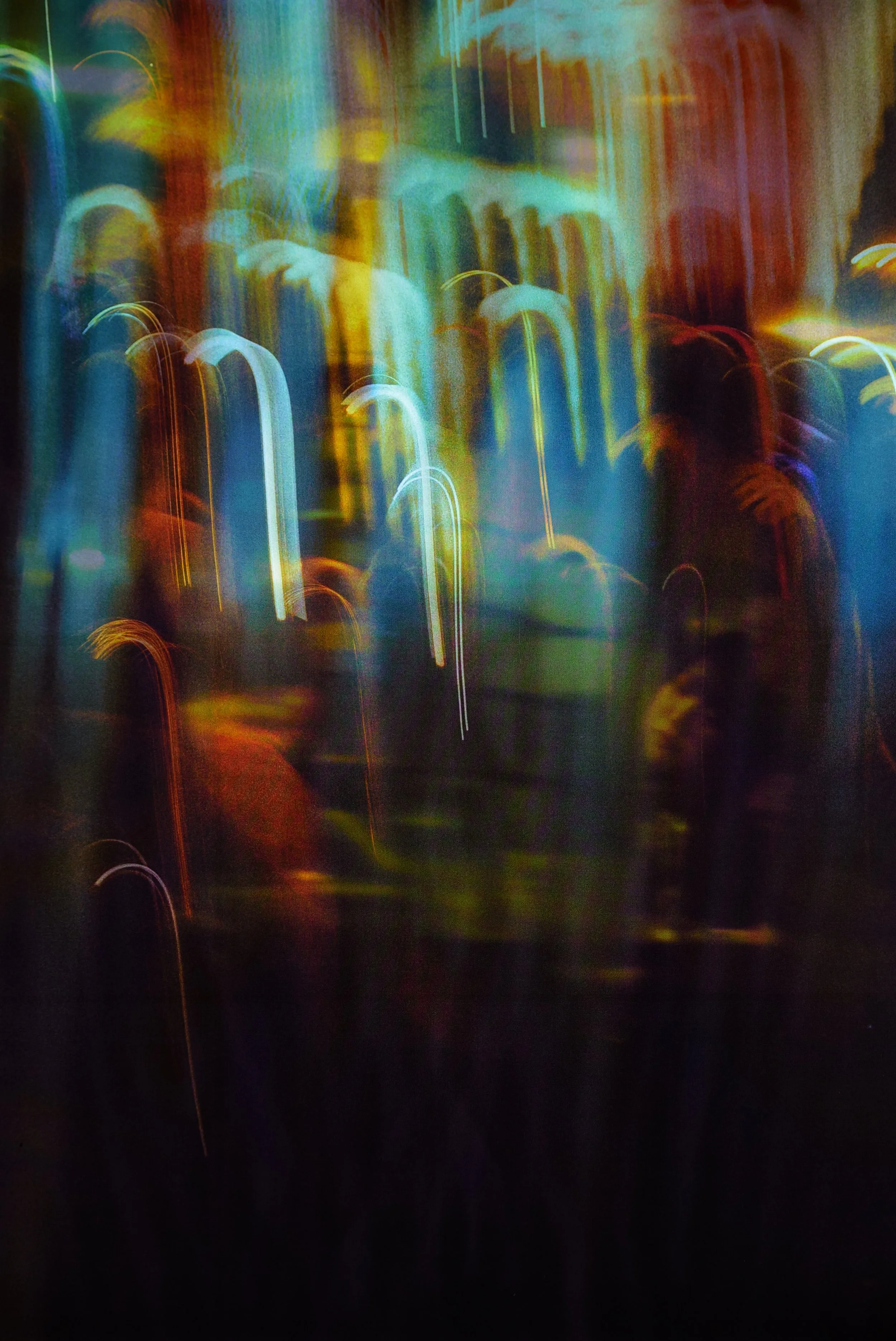 Ember Veil

Two nights lie on top of each other here. At the bottom of the image, behind the soft cloud of a plastic tarp, a woman leans very slightly into the person beside her. The restaurant is almost all colour and blur from where I’m standing; t