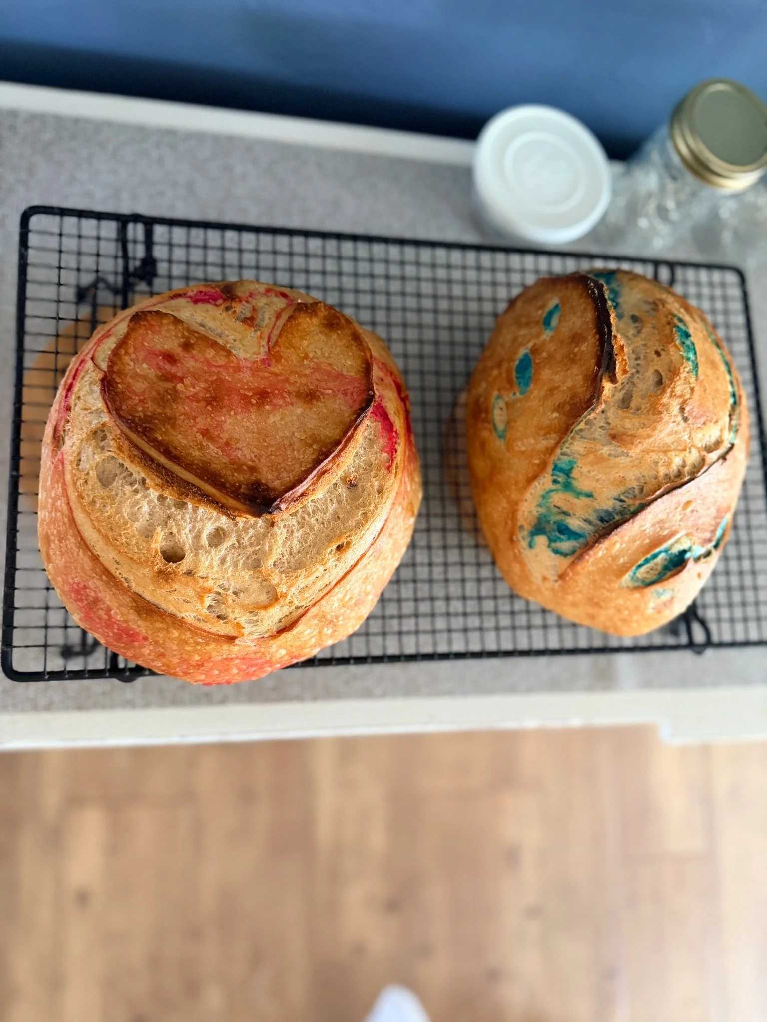 Two baked goods on a wire rack, with one resembling a muffin with a heart-shaped topping and the other a muffin with colorful patches.