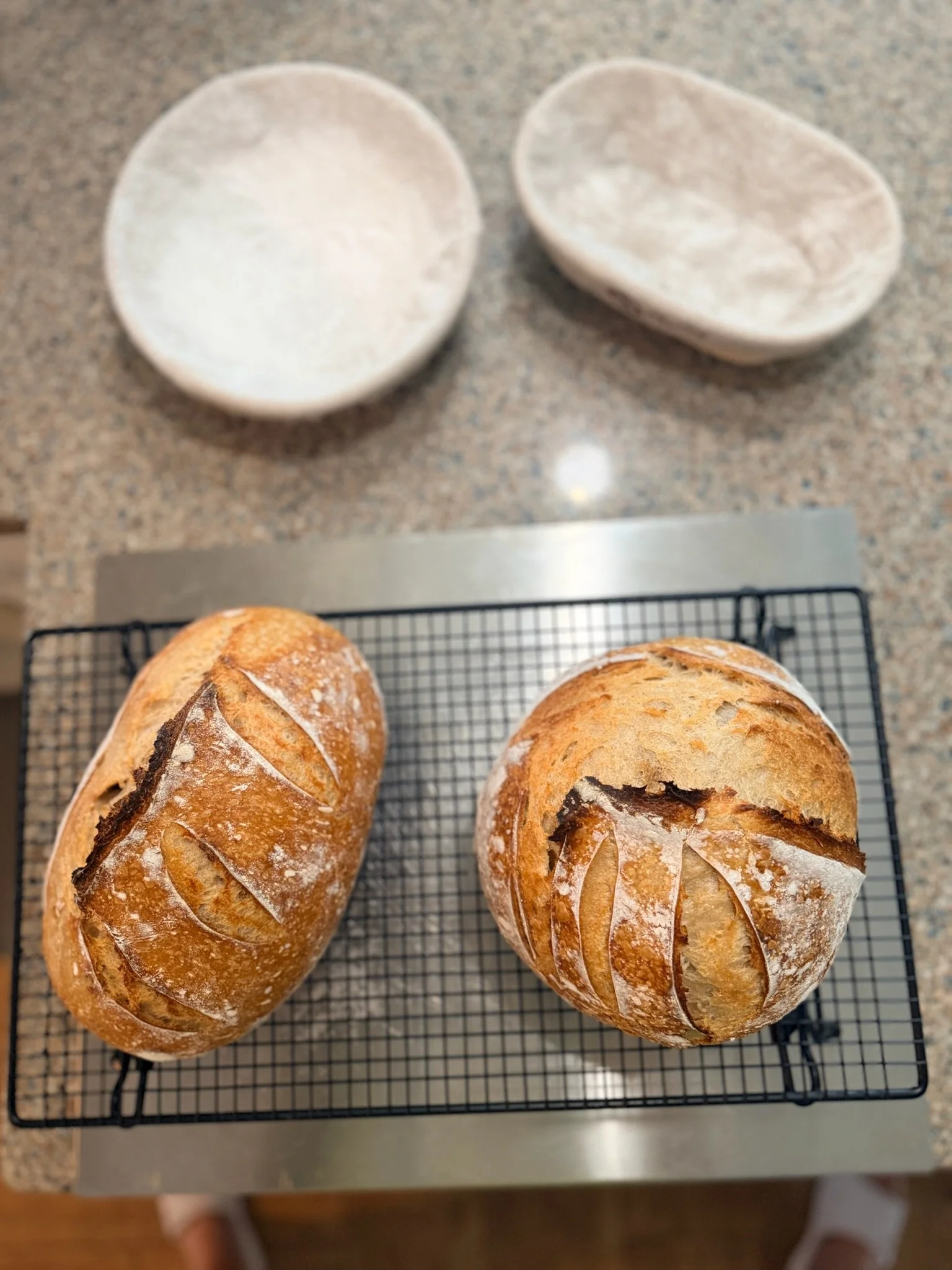 Two freshly baked round bread loaves with scoring patterns on top, resting on a wire cooling rack.