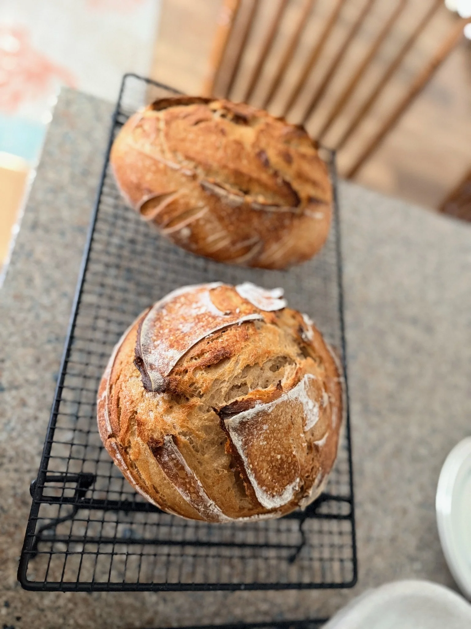 Two loaves of freshly baked bread with a golden crust and visible swirls of filling, cooling on a black wire rack on a gray countertop.