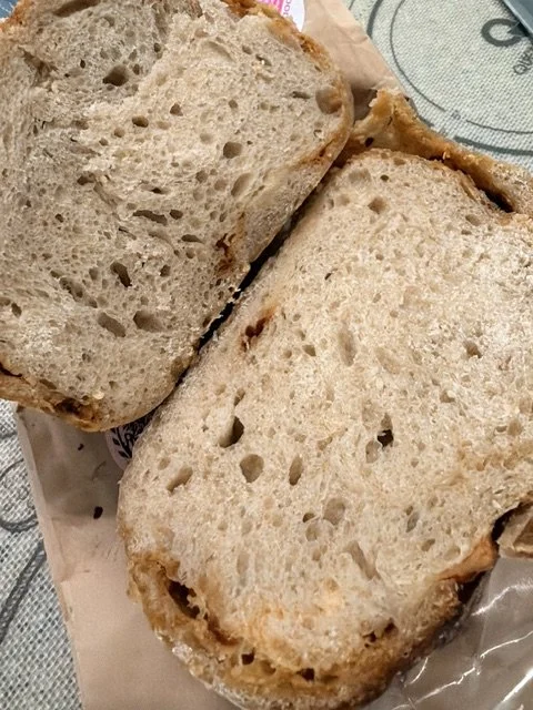 Two halves of a sandwich bun with sesame seeds on the crust, resting on a paper wrapper.