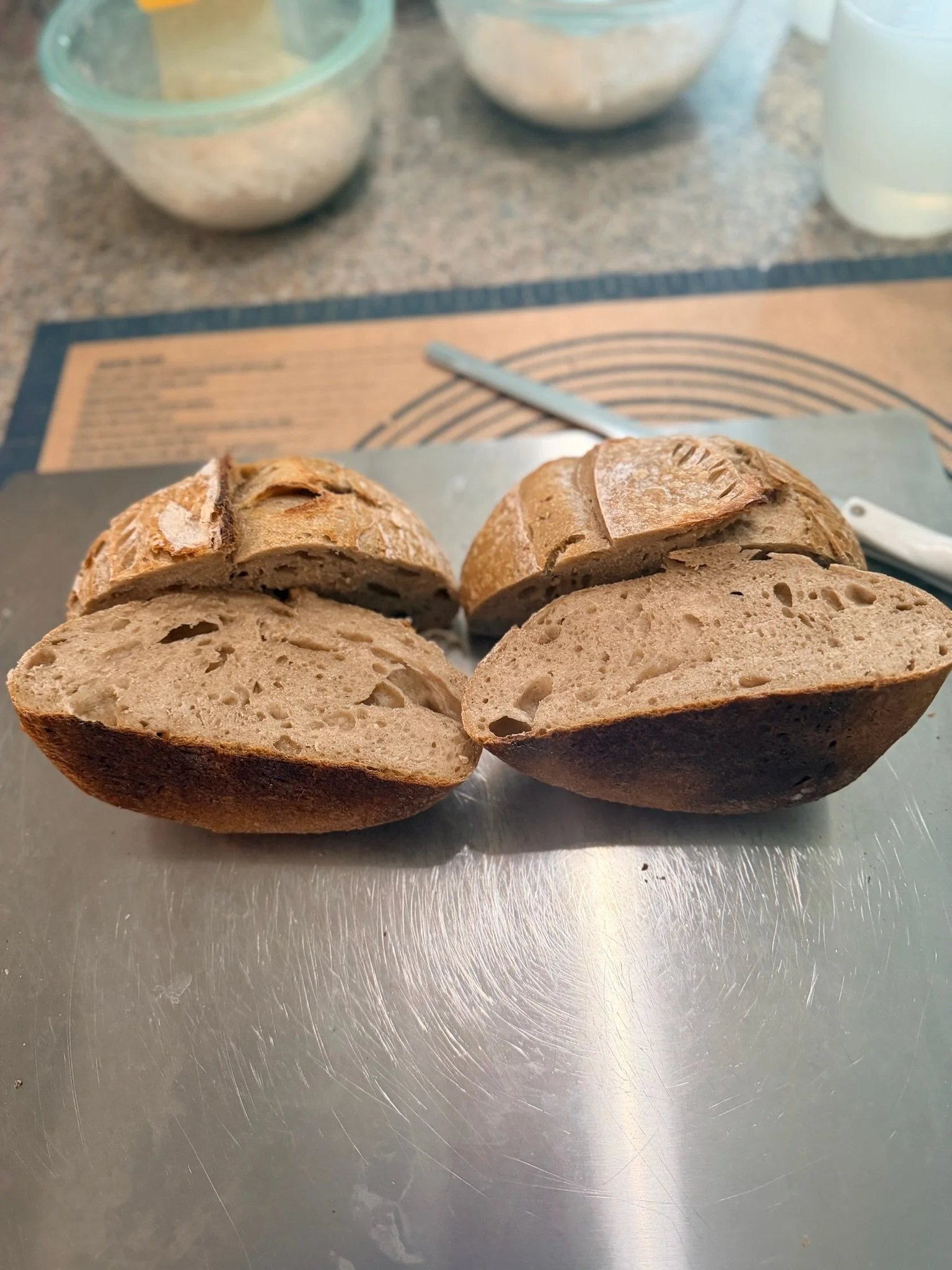 Two halves of a loaf of bread with a crusty exterior and soft interior, placed on a metal surface in a kitchen setting