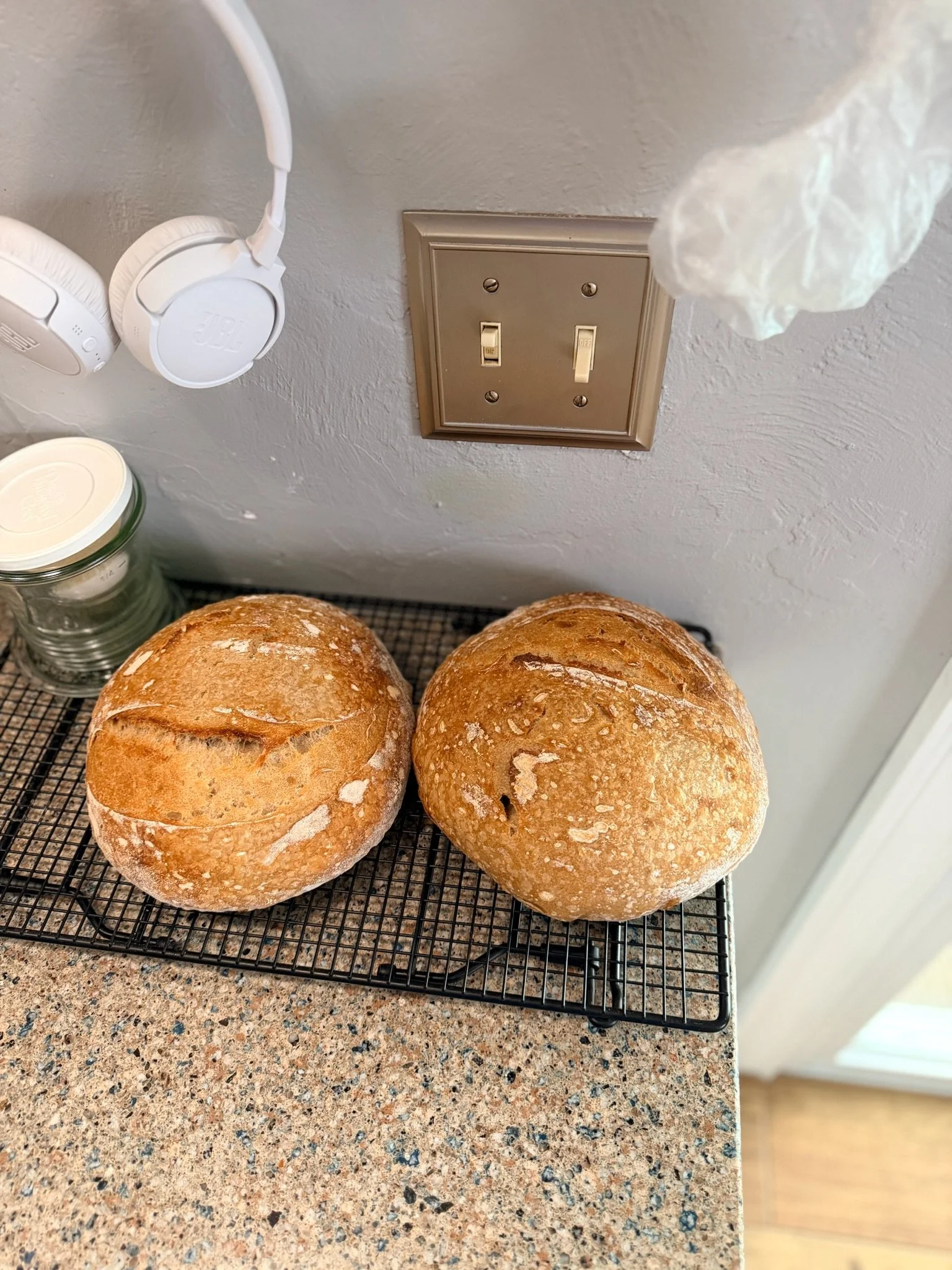 Two freshly baked round bread loaves with a golden crust on a wire cooling rack on a speckled countertop.