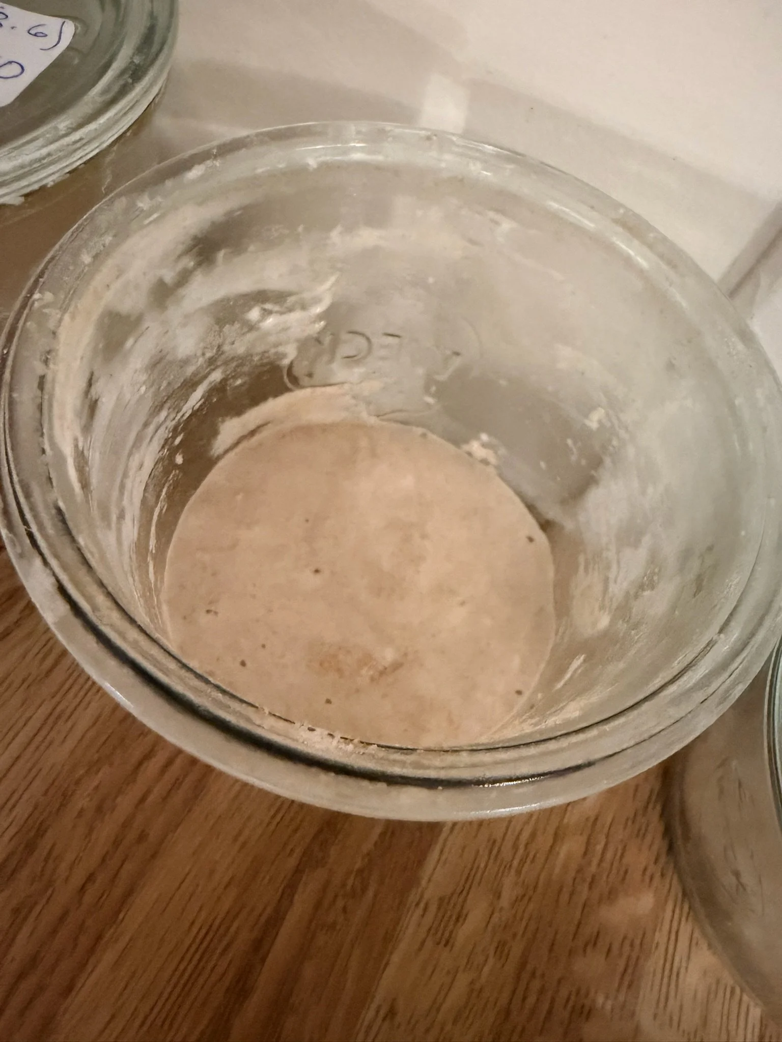 Empty glass jar with residual powder or flour on the inside, placed on a wooden surface.