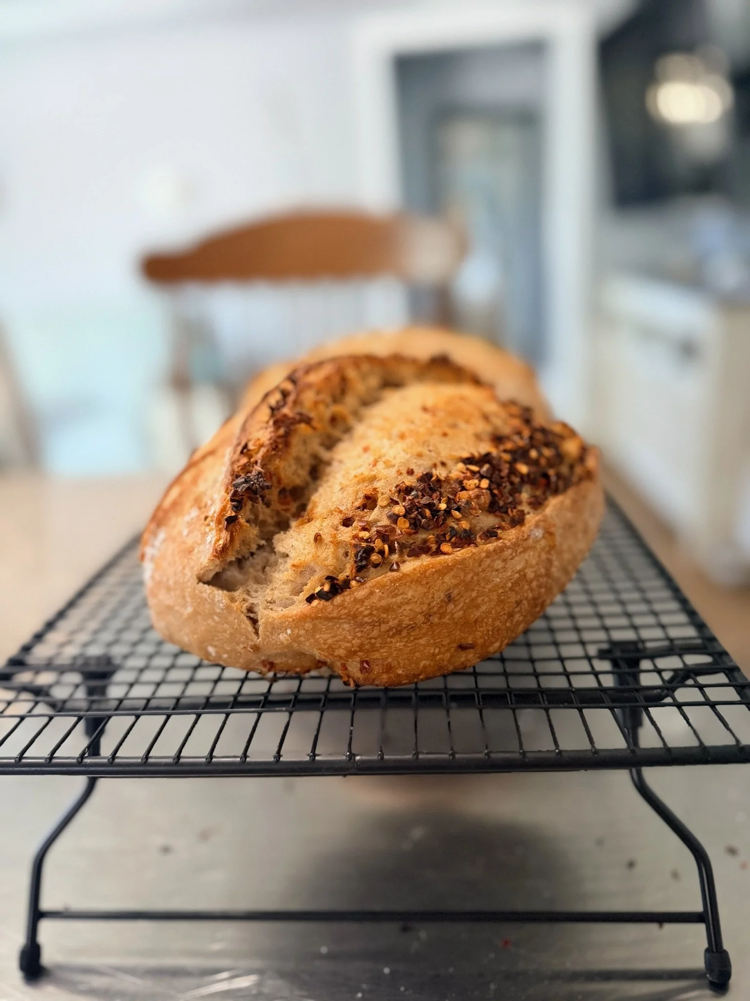Close-up of a freshly baked bread with a crust covered in spices, resting on a cooling rack in a kitchen.