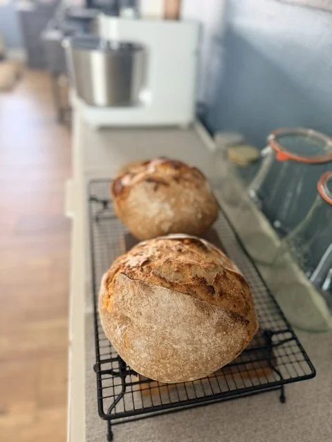 Two loaves of freshly baked bread cooling on a wire rack in a kitchen.