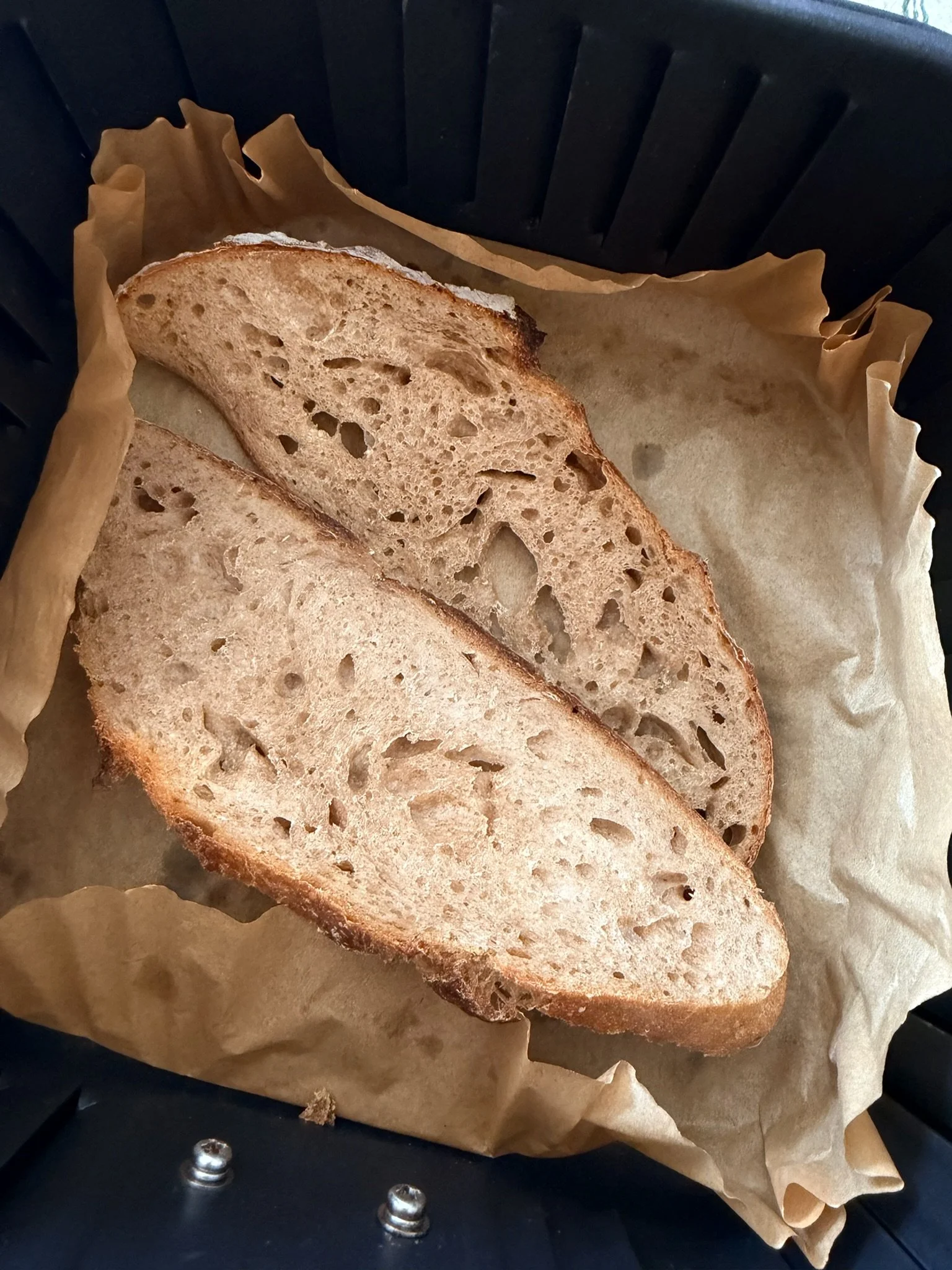 Slices of toasted bread on parchment paper in a black toaster oven.