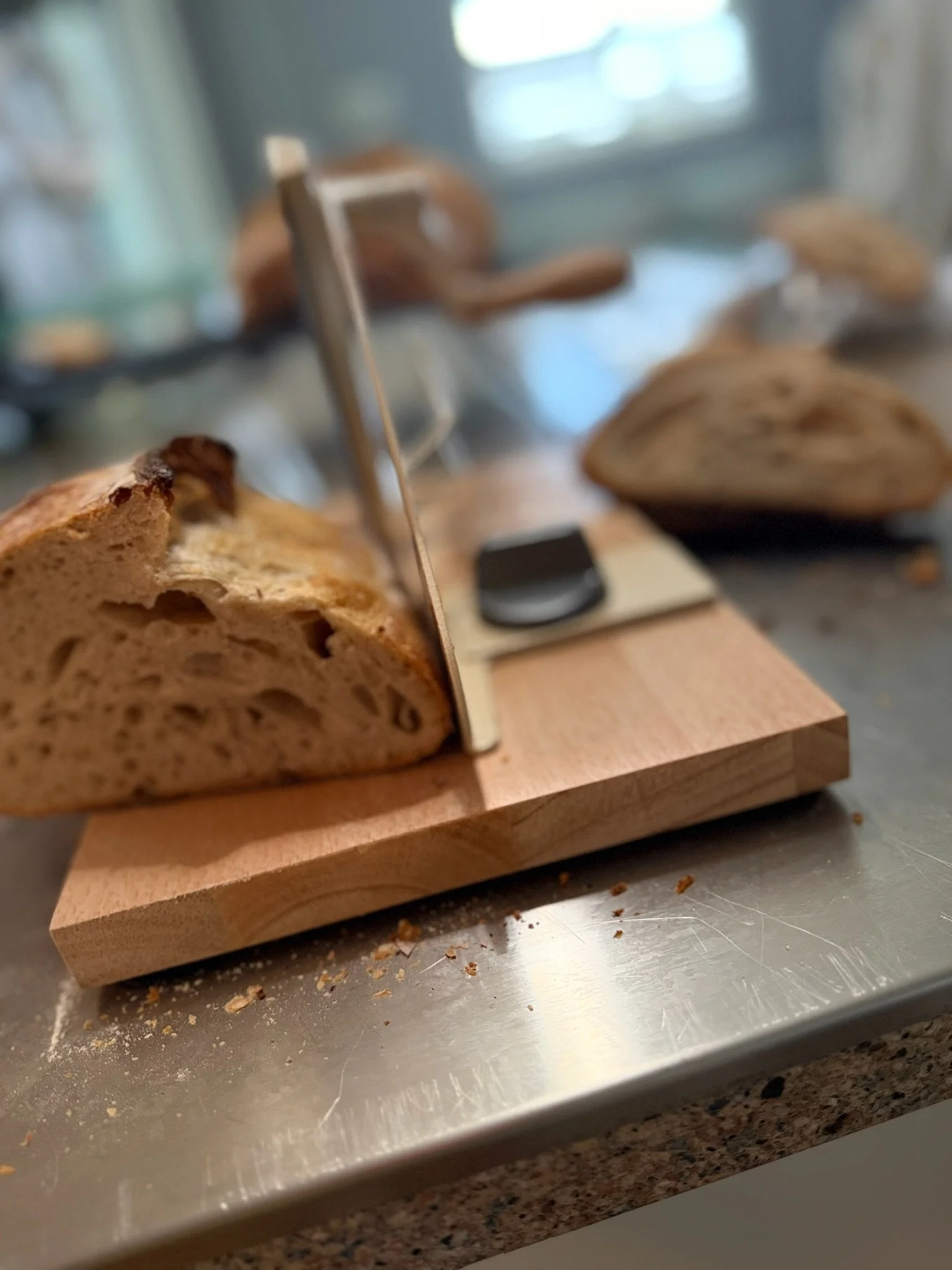 Slices of bread on a wooden board with a metal surface and crumbs around; blurred background.