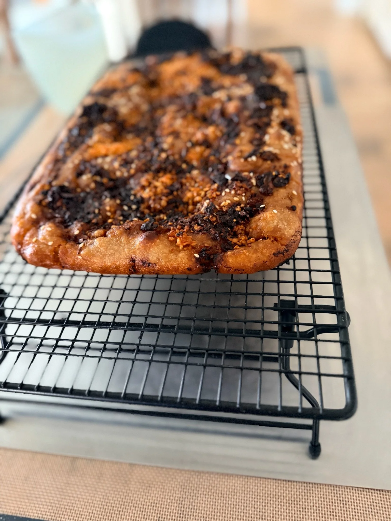 A loaf of bread topped with chocolate chunks and sprinkled with sesame seeds, cooling on a black wire rack.