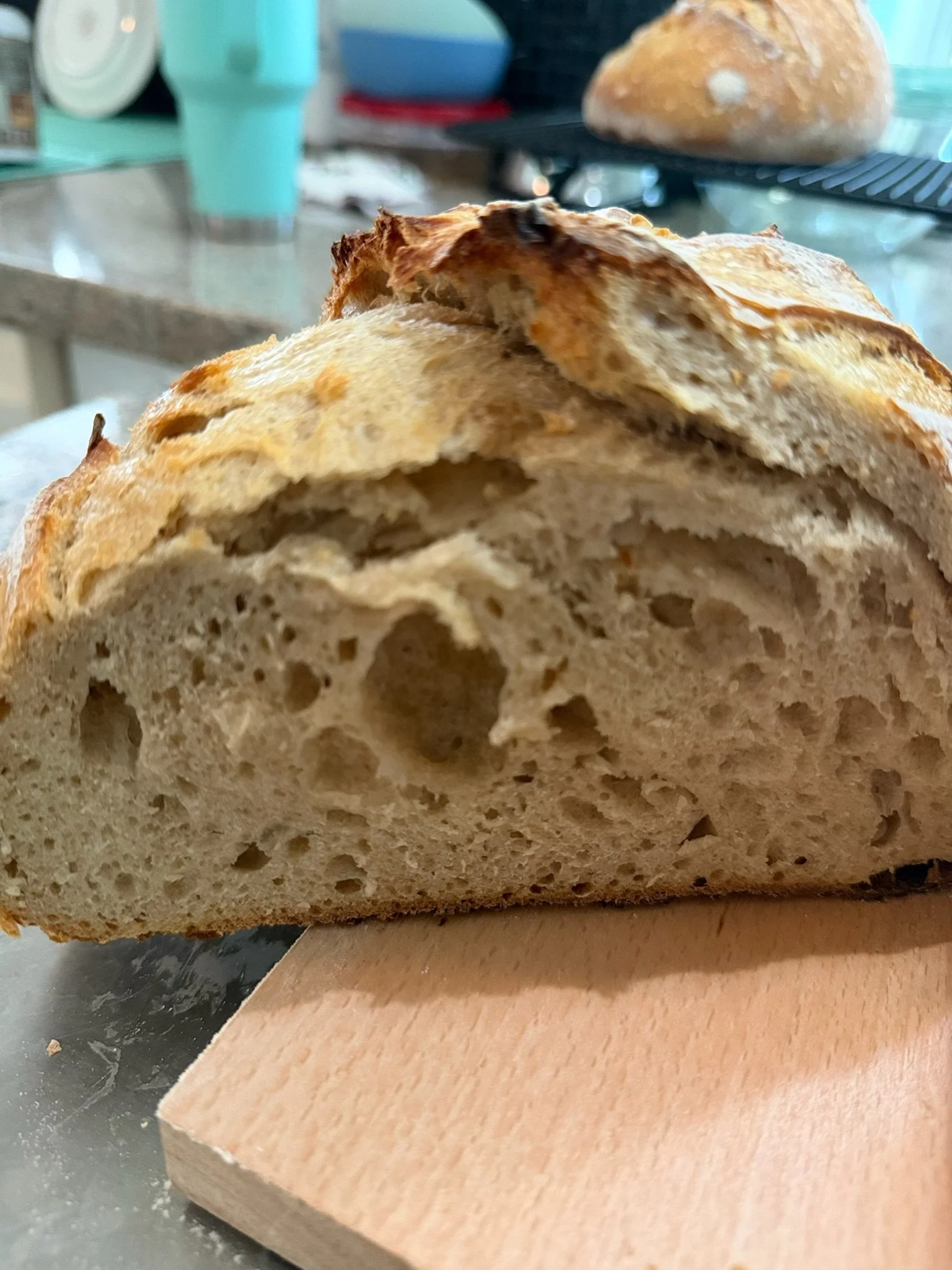 Close-up of a cut loaf of rustic bread on a wooden cutting board, with a blurred kitchen background.
