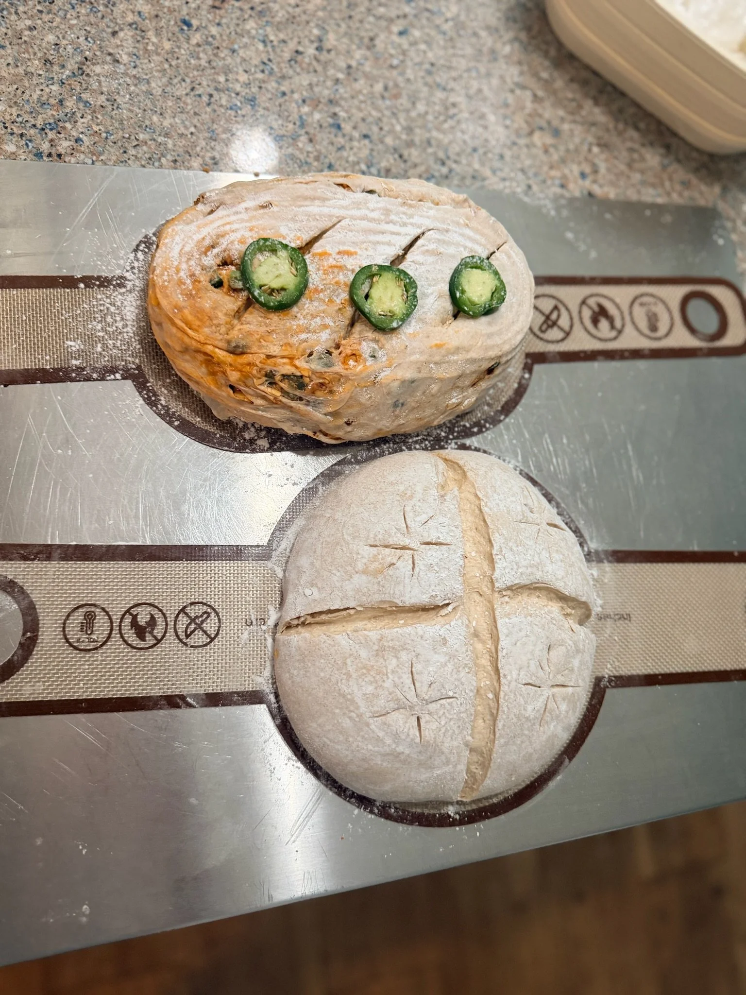 Ball of dough topped with three slices of jalapeno peppers, resting on a silicone baking mat on a countertop.