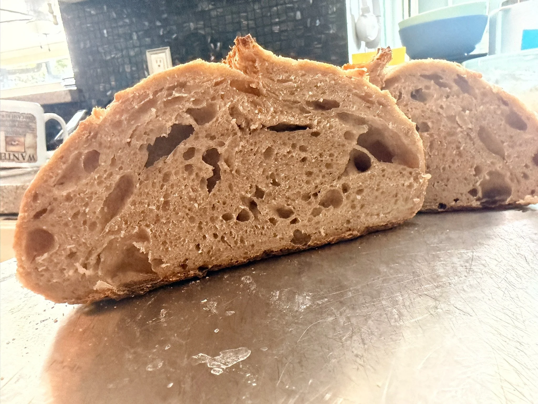 Close-up of a sliced loaf of bread on a reflective surface in a kitchen setting.