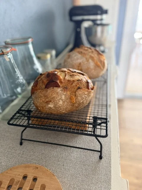 Two freshly baked bread loaves cooling on a wire rack in a kitchen setting.