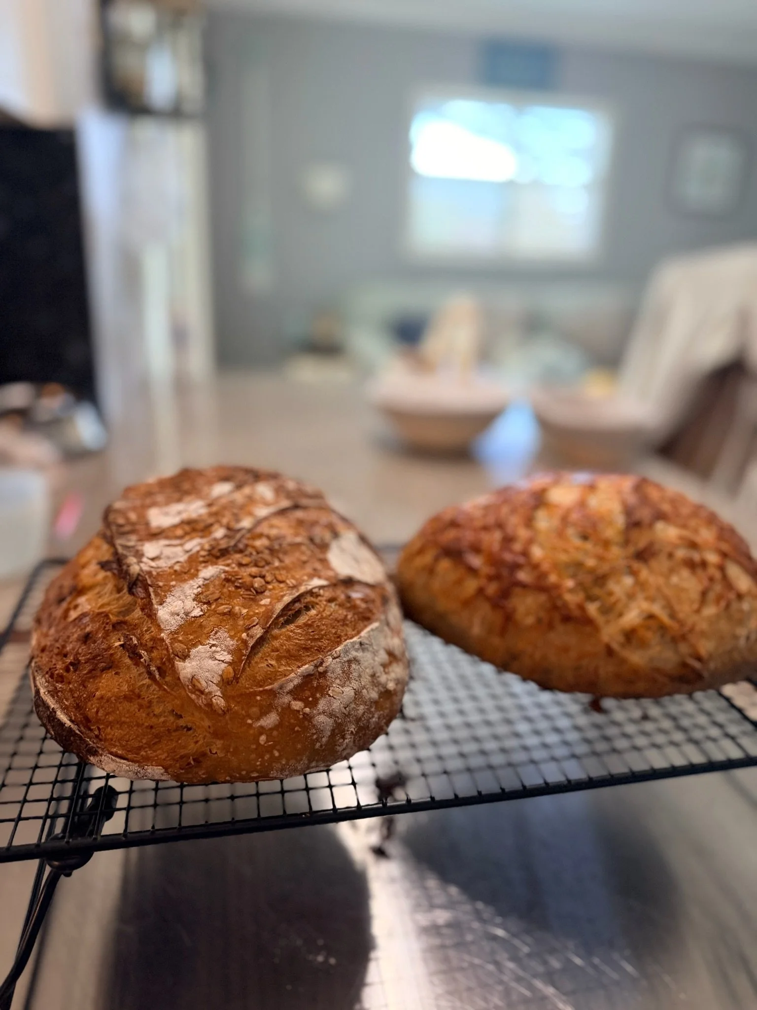 Close-up of two freshly baked bread loaves resting on a wire cooling rack in a kitchen.