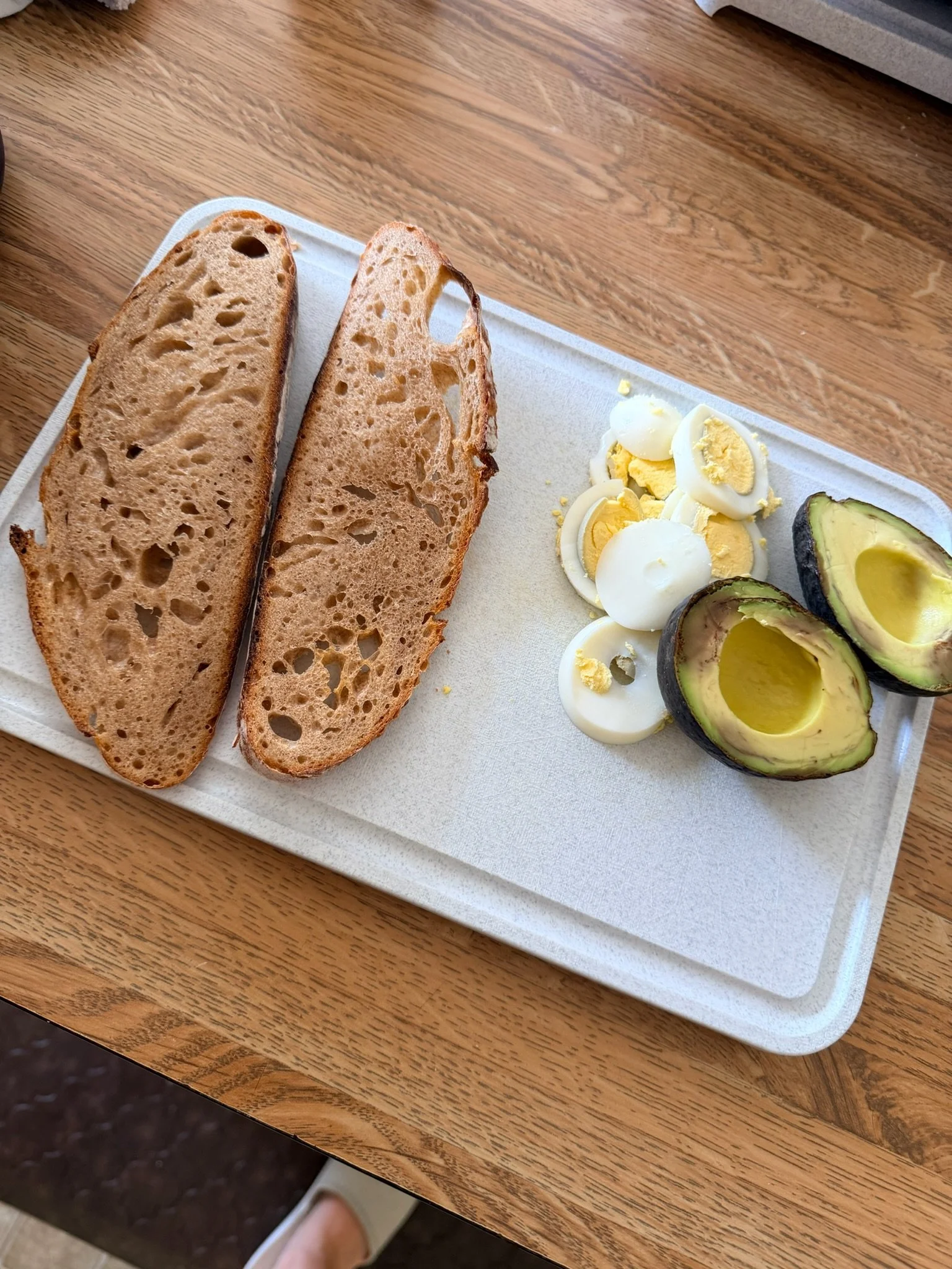 Sliced bread, sliced hard-boiled eggs, and sliced avocados on a white foam plate on a wooden table.