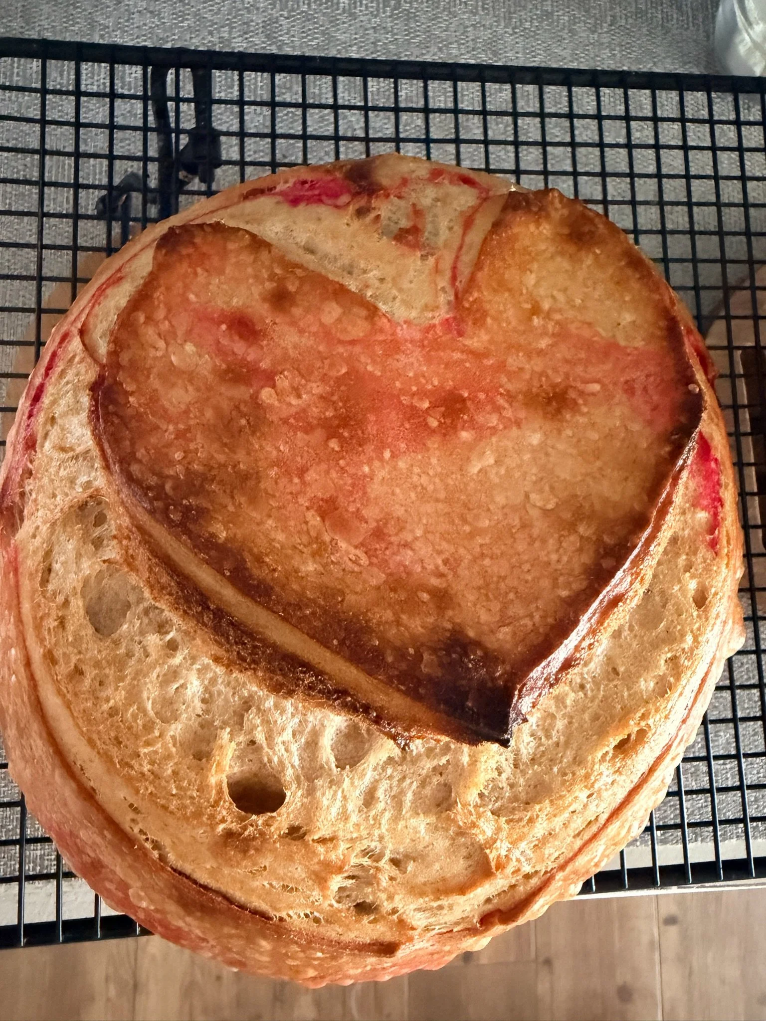 Close-up of a large slice of cooked ham with a light brown crust, placed on a black wire cooling rack.