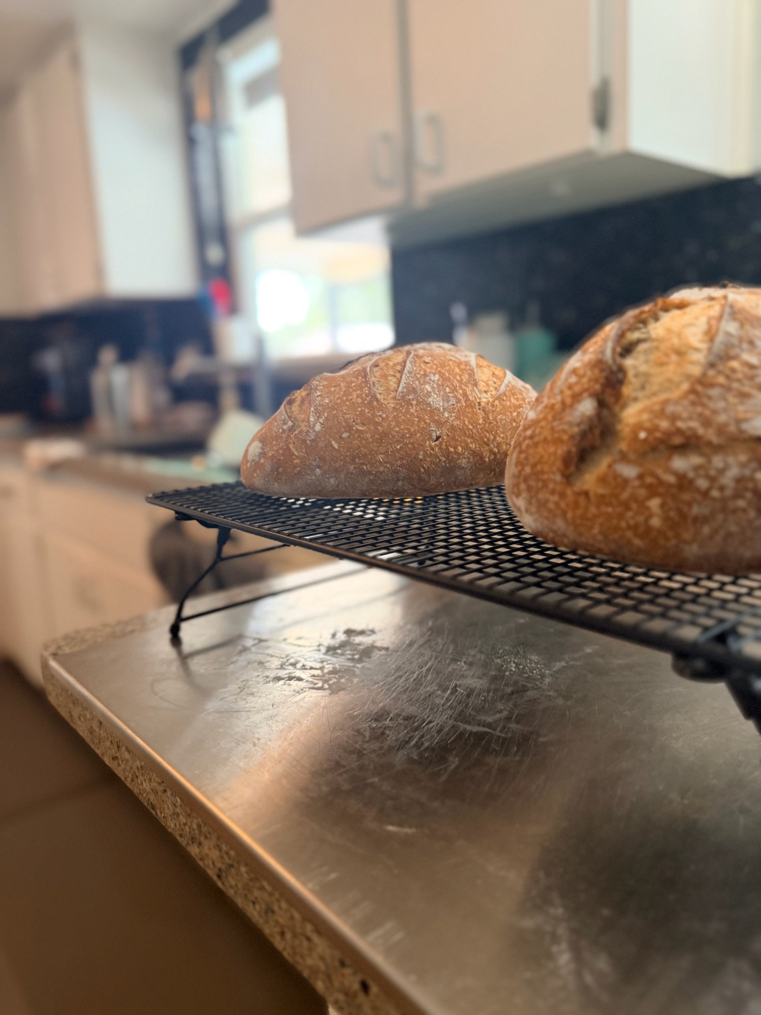 Two loaves of bread cooling on a wire rack on a kitchen countertop.