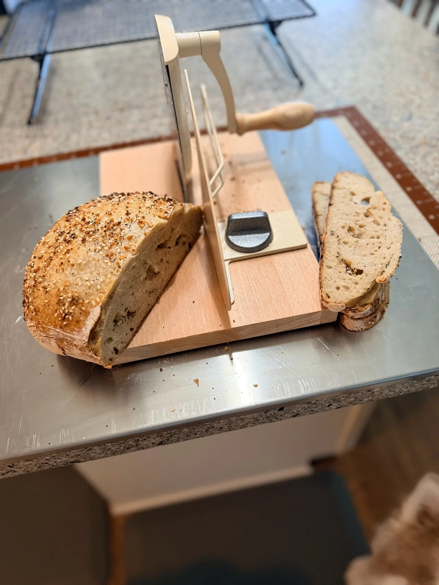 A loaf of bread on a wooden bread slicing guide with a serrated bread knife and two slices of bread on the right side of the guide, placed on a kitchen countertop.