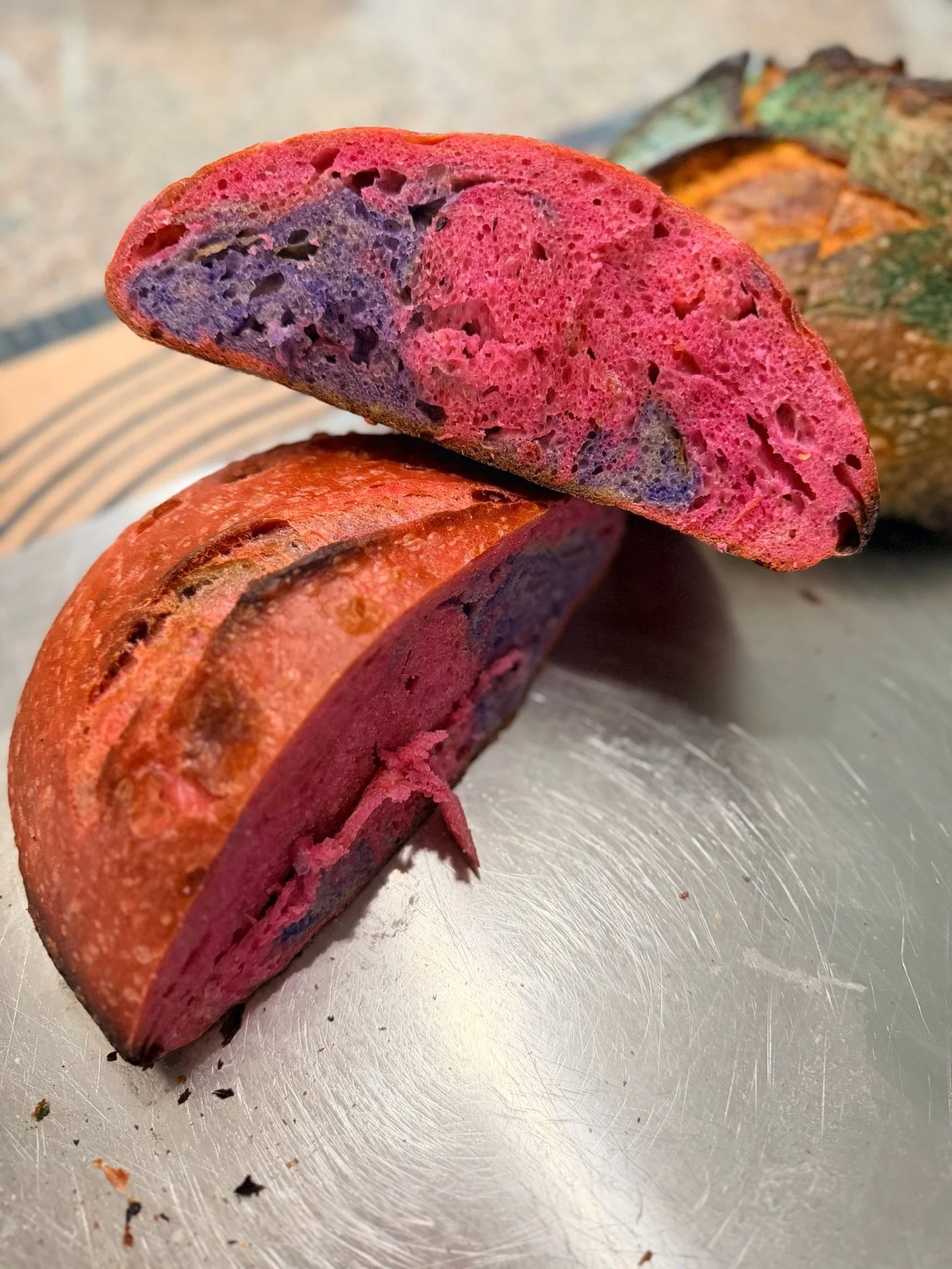 Close-up of a sliced colorful sausage on a silver surface, revealing a marbled interior with pink, purple, and green hues.