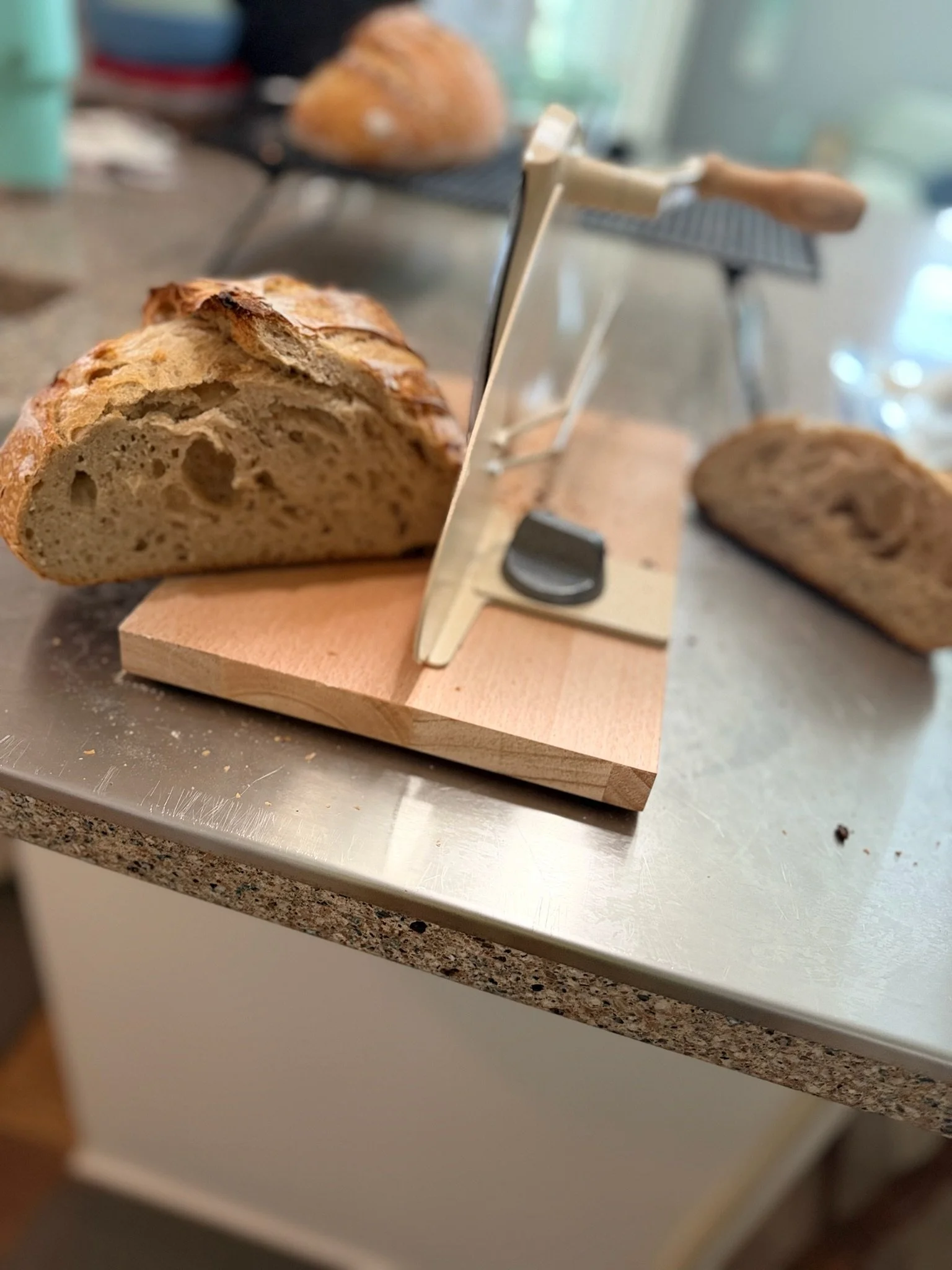 A loaf of bread partially sliced on a wooden cutting board, with a bread slicing guide in use, on a kitchen countertop.