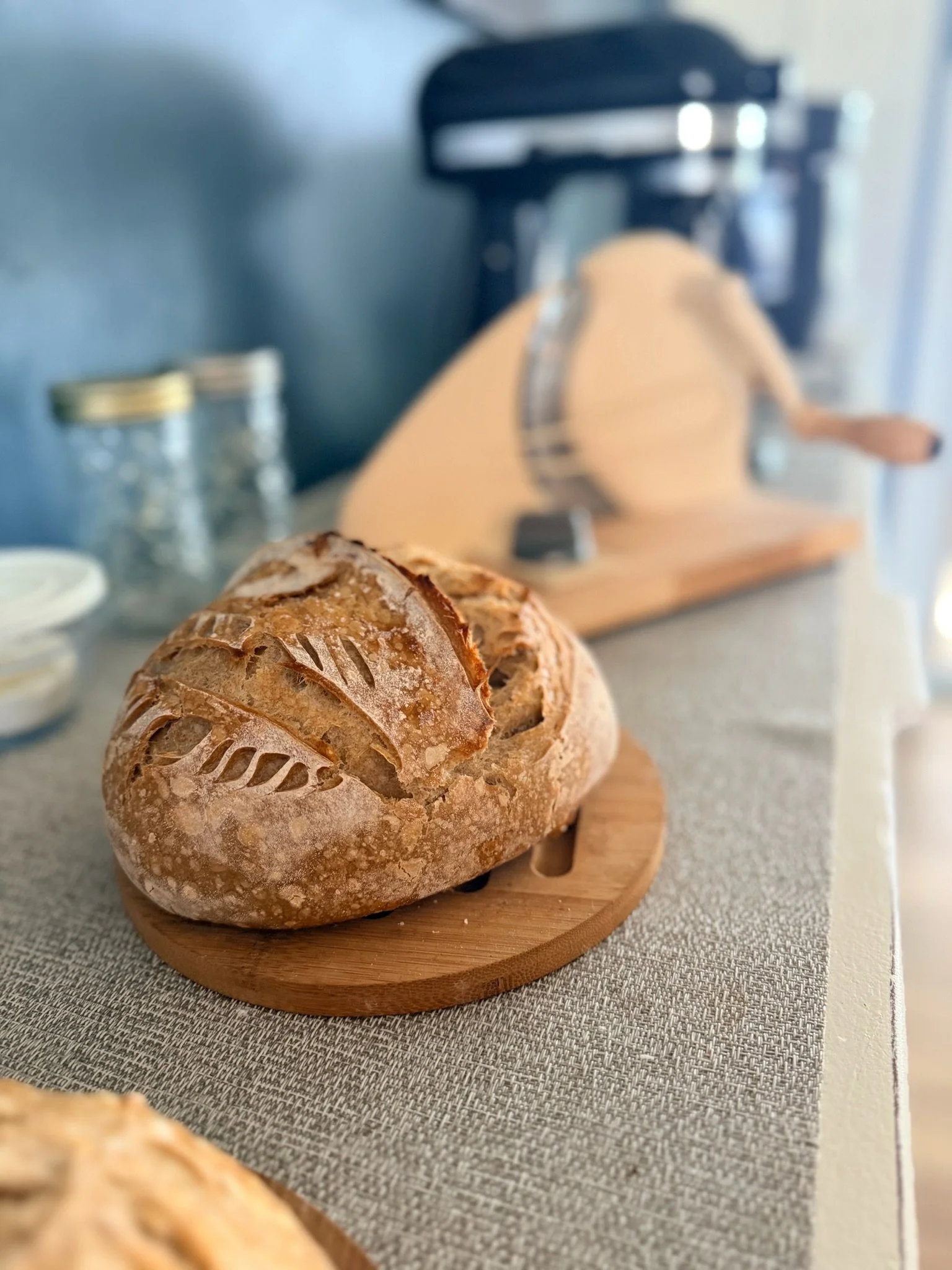 Close-up of a round loaf of bread with a decorative scored crust on a wooden serving board.